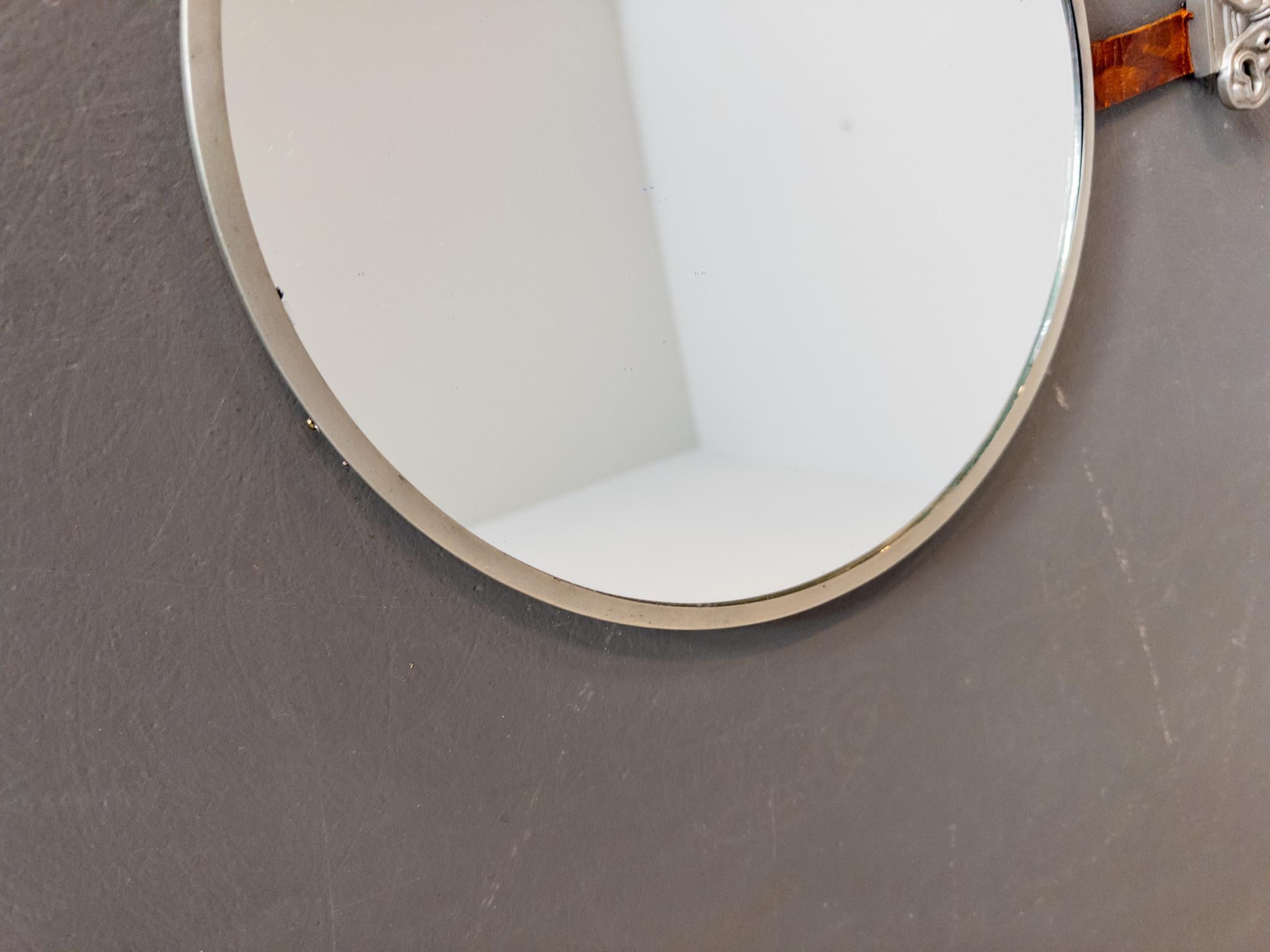 Ce superbe et rare miroir, conçu par Hans Bergström pour Ystad-Metall en 1932, est une véritable pièce de collection. Doté d'un couvercle en étain avec les masques emblématiques de la comédie et de la tragédie, d'une sangle en cuir patiné et d'un