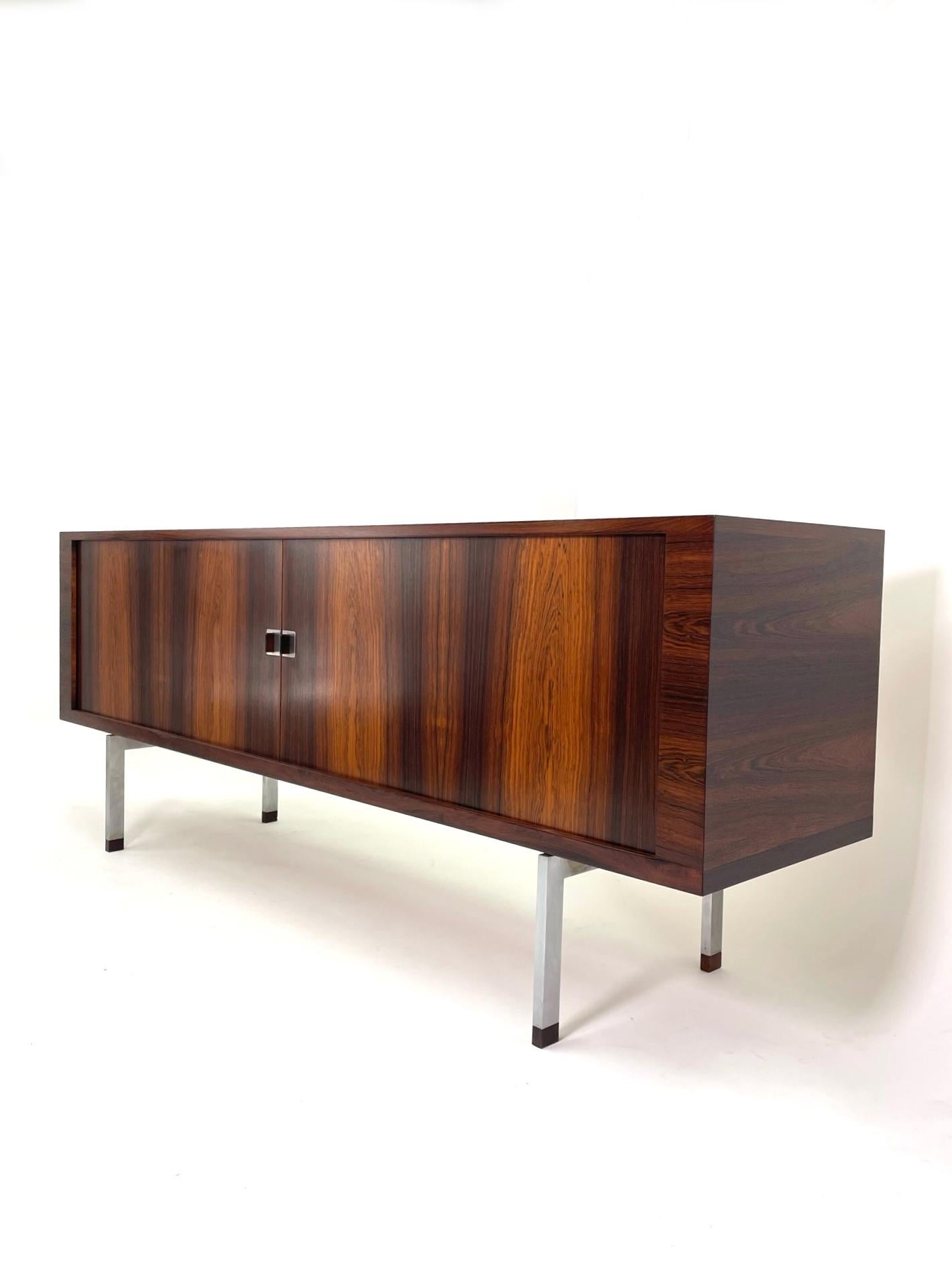 The rarest and most sophisticated cabinet designed by the master of Danish Modern design executed in Brazilian rosewood and white oak. This exquisite credenza sits on brushed stainless steel legs that are capped in solid rosewood. This is the caviar