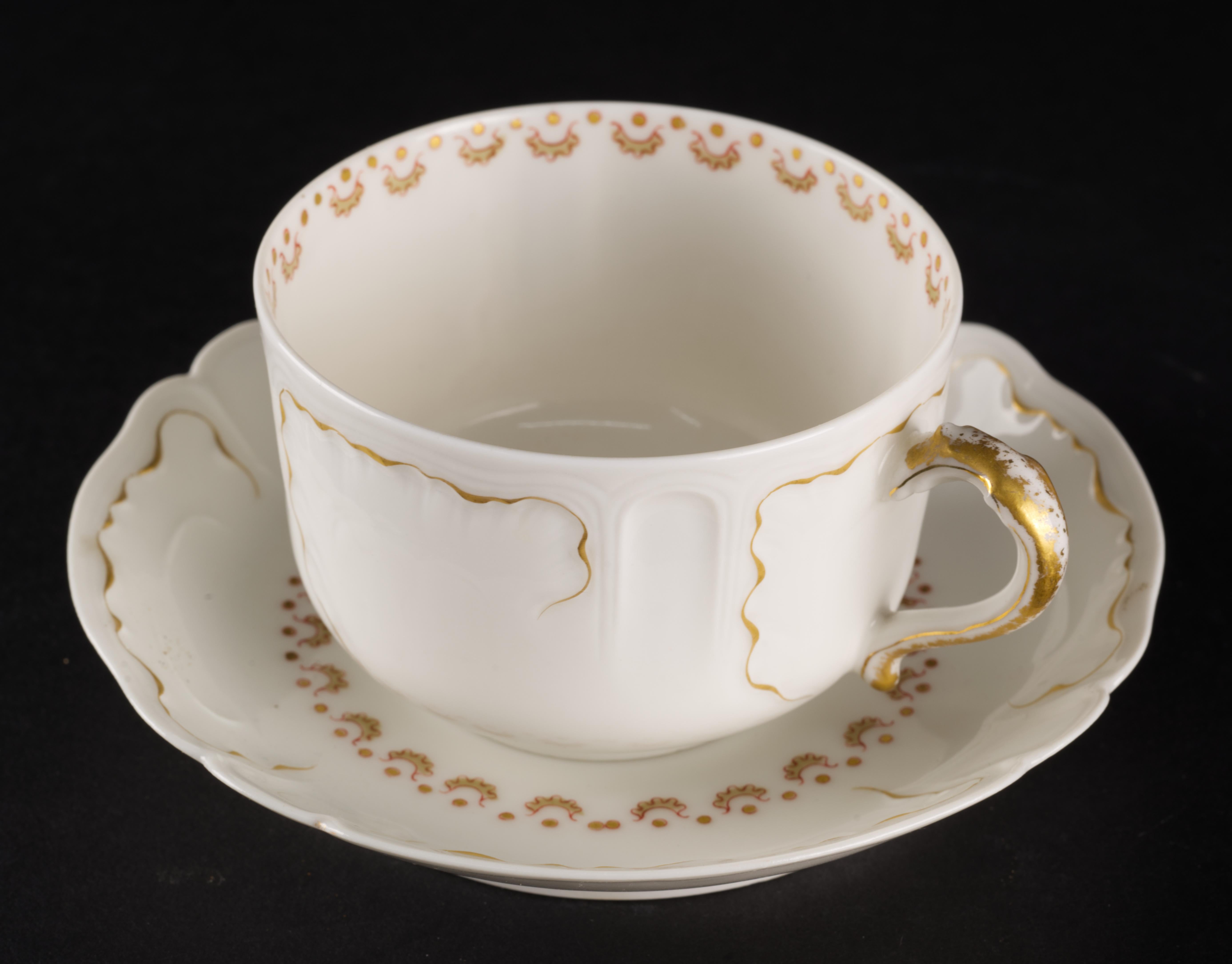 
Le service de tasses et soucoupes de Limoges a été fabriqué en porcelaine fine et semi-translucide et décoré à la main dans une délicate palette d'or, de rouge foncé et de gris pâle. Les contours en or ont été utilisés pour rehausser les formes