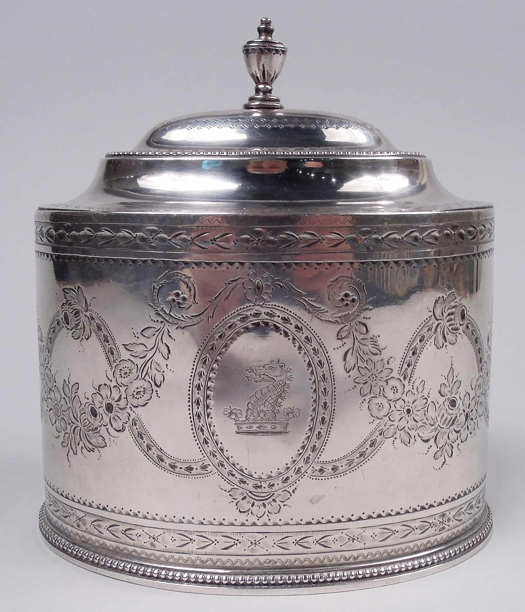 George III sterling silver tea caddy. Made by Hester Bateman in London in 1782. Straight oval bowl; cover domed with cast vasiform finial. Engraved garland and swag and ornamental borders. Beading. Beautiful Neoclassicism for a special blend. Fully