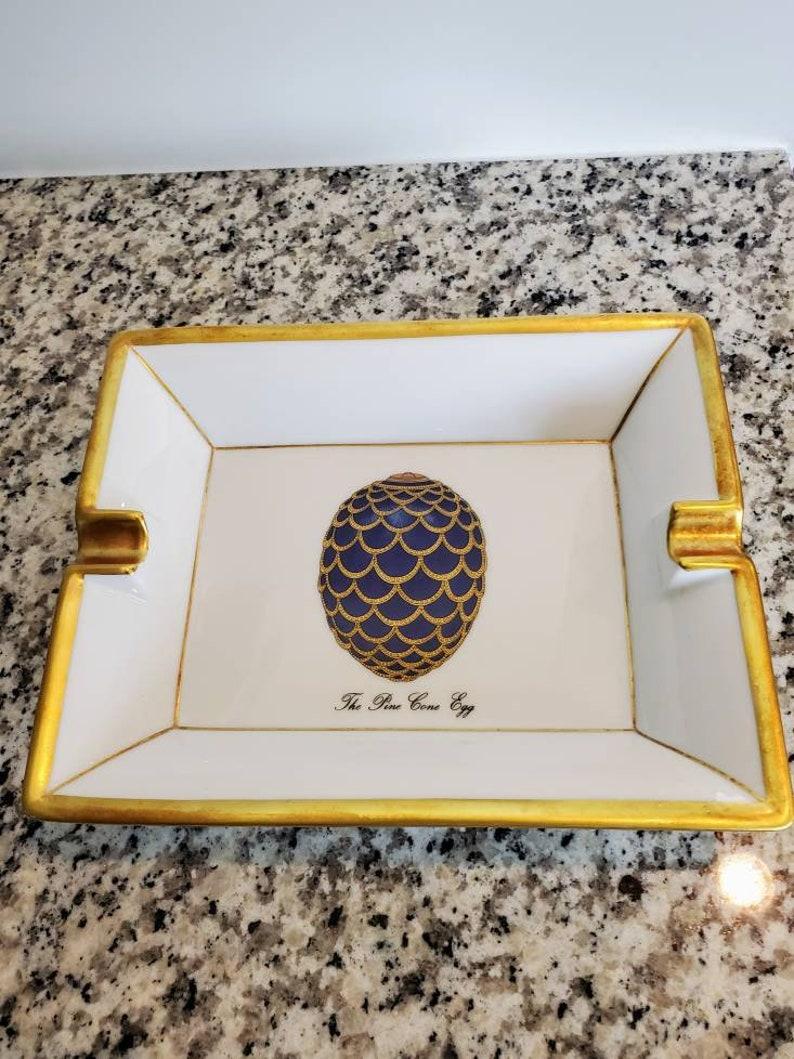 Créé exclusivement par la Maison Fabergé et la porcelaine de Limoges en France, nous sommes fiers d'offrir ce fabuleux plateau en porcelaine de qualité supérieure, peint à la main et rehaussé d'or doré, richement décoré d'un œuf de pomme de pin