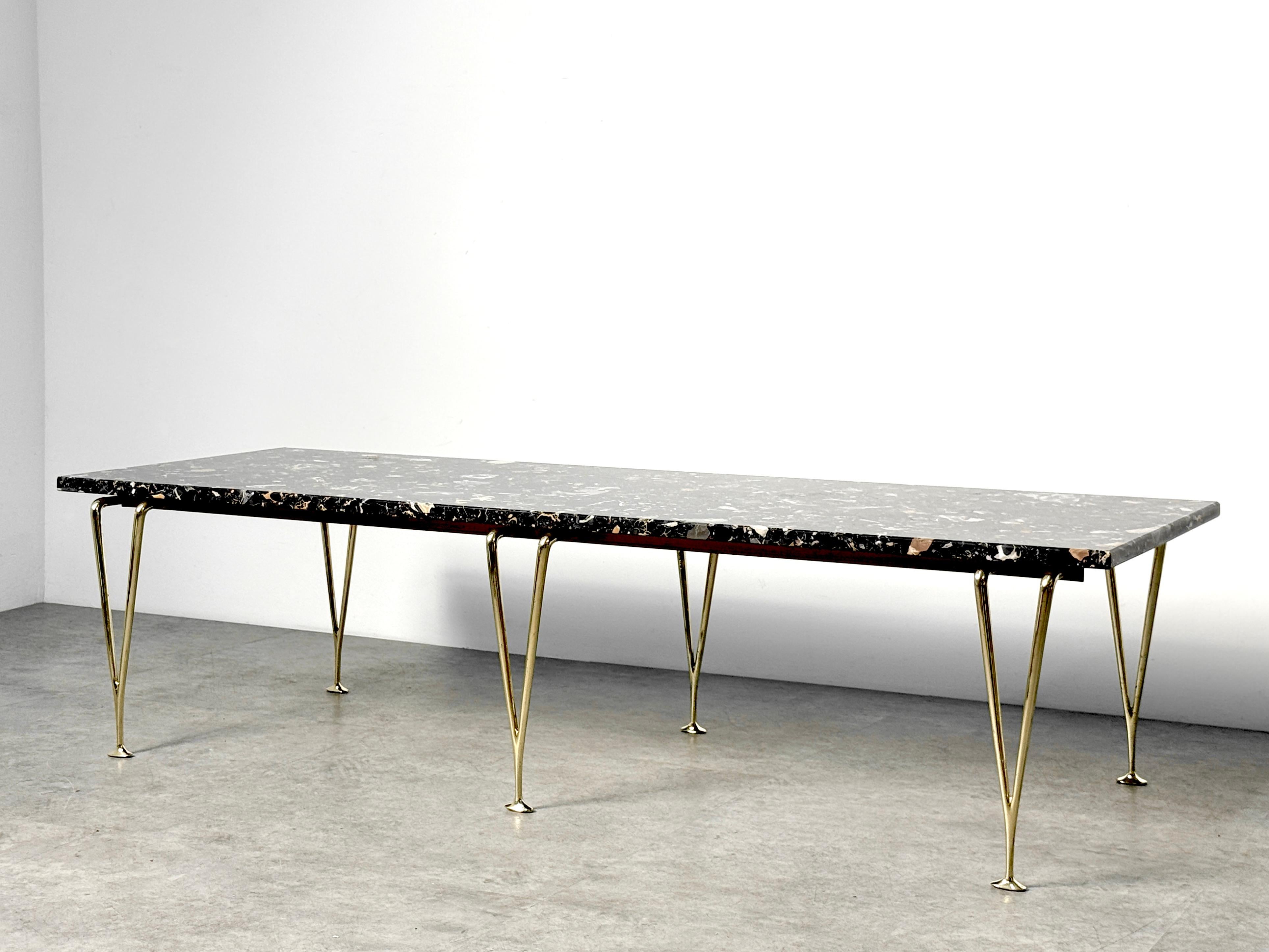 Rare table à plateau de marbre noir en terrazzo conçue par Hughes Acton vers la fin des années 1960.

Surface rectangulaire originale en terrazzo noir massif soutenue par six pieds sculpturaux en laiton poli.

Une adaptation sophistiquée de la