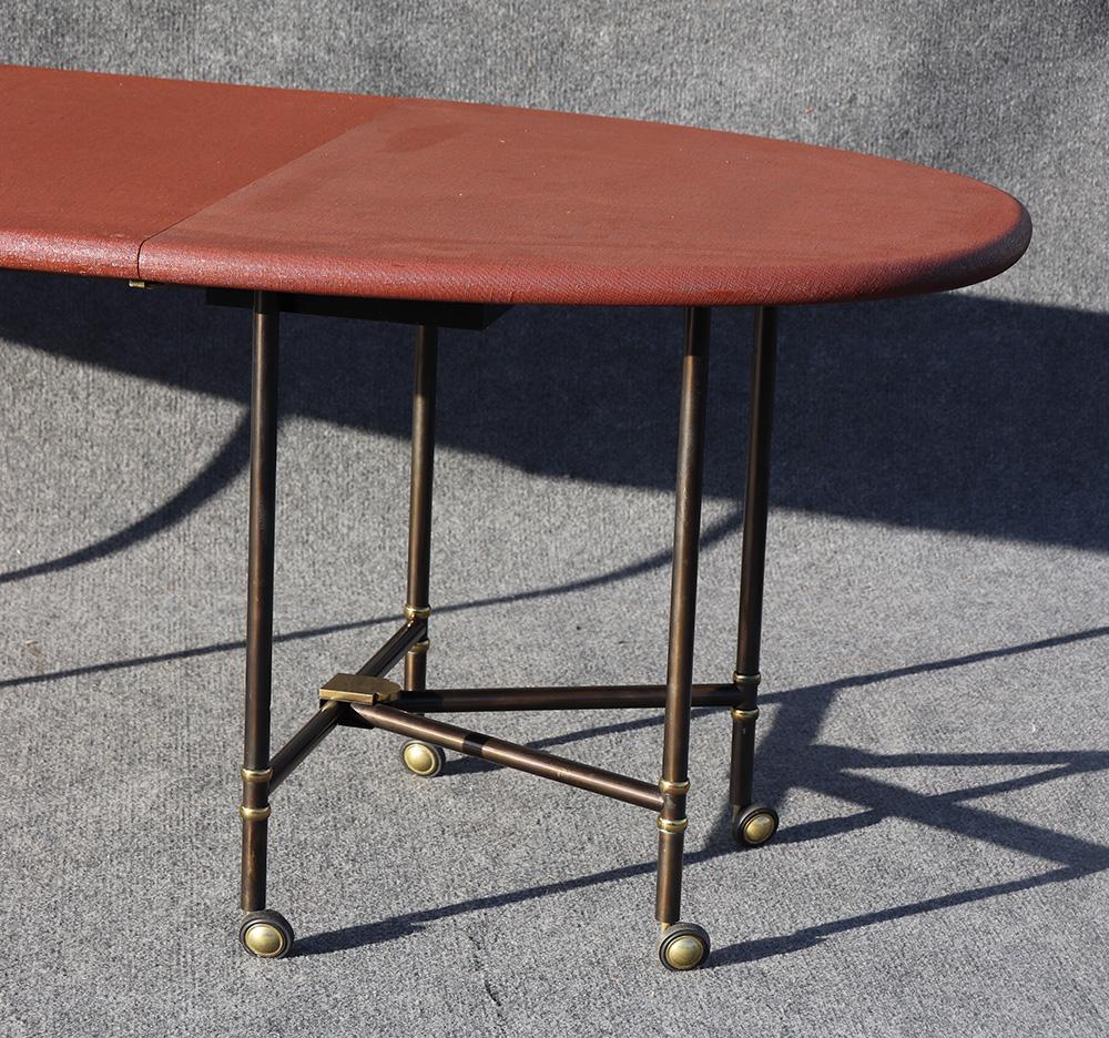 This is perhaps Maison Jansen's most iconic design ever made. This incredibly rare table, of which only a dozen or less are even in the world. This is a foldable dining table, that has a canvas texture and gunmetal steel and brass folding legs with