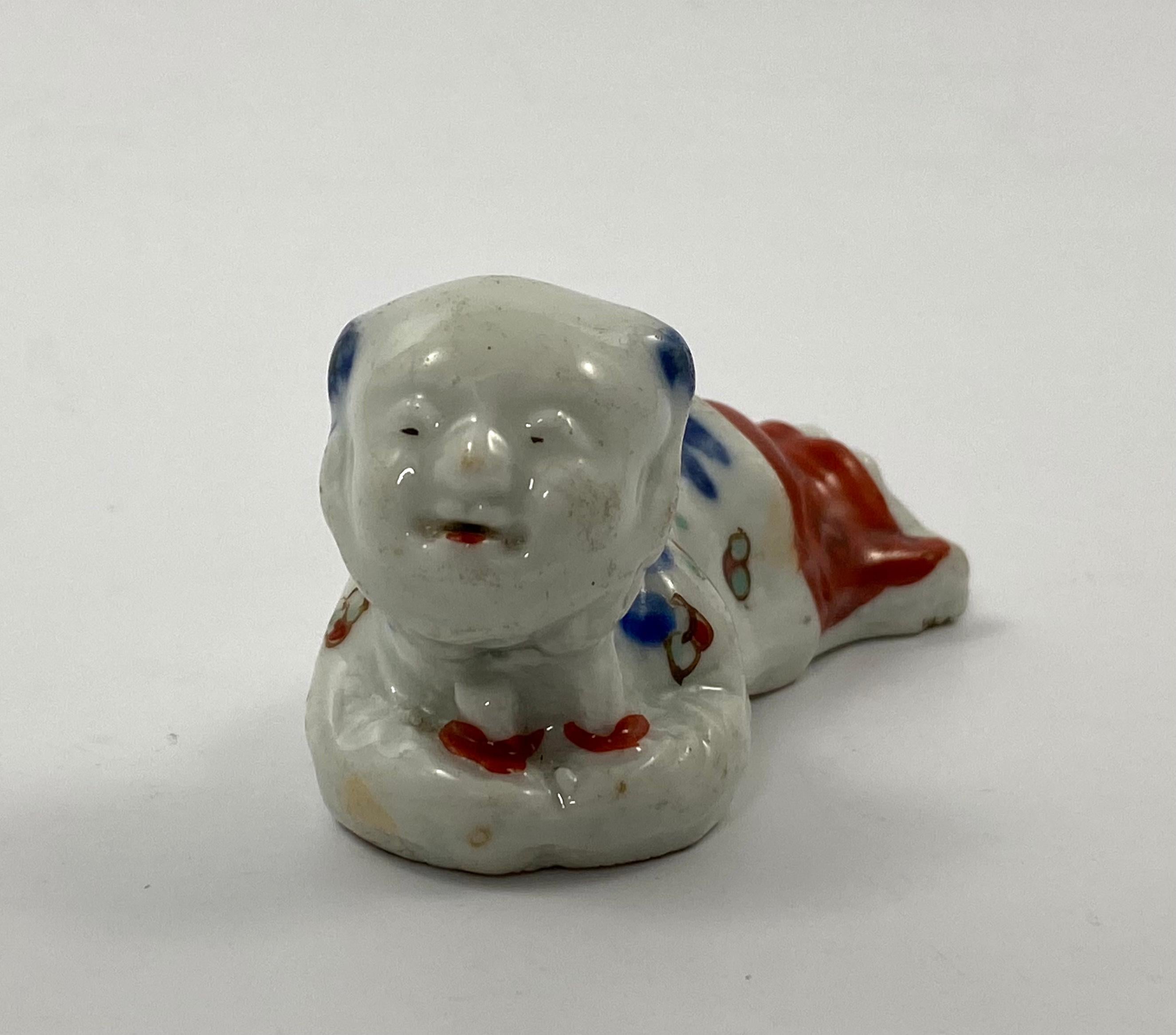 Rare Arita porcelain bird whistle, Japan, c. 1690, Edo Period. Taking the form of a reclining boy, resting his head in his hands. His tunic enamelled in Imari style, with flowers.
The whistle is blown through a slot in his feet, with the sound