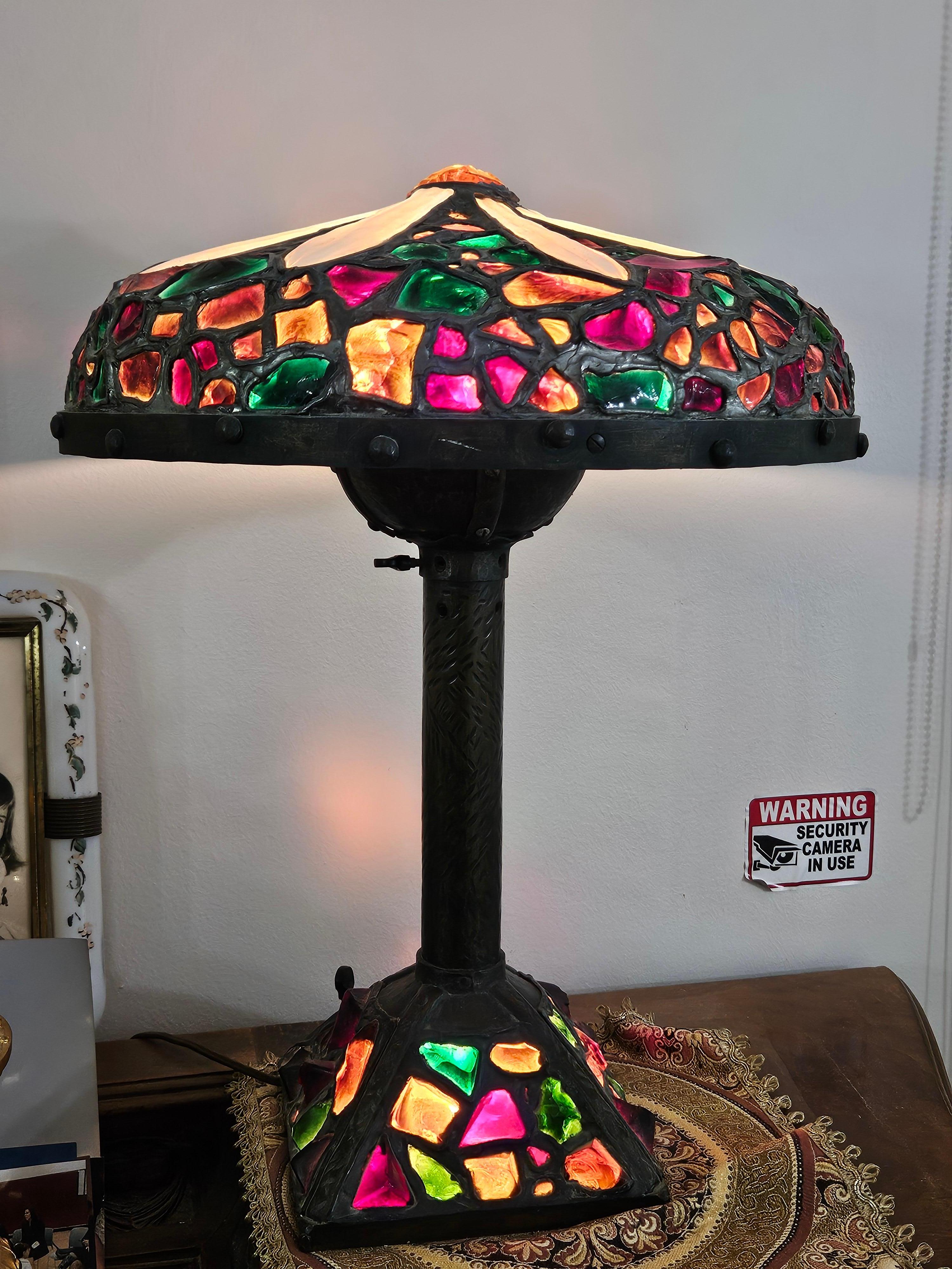 The Following Item we are offering is this Beautiful Rare Early 1900s Bronze Chunk Glass and jewel table lamp. This large shade is made of many colors including rich ruby reds, emerald greens, deep amber glass jewels, with opalescent glass on top