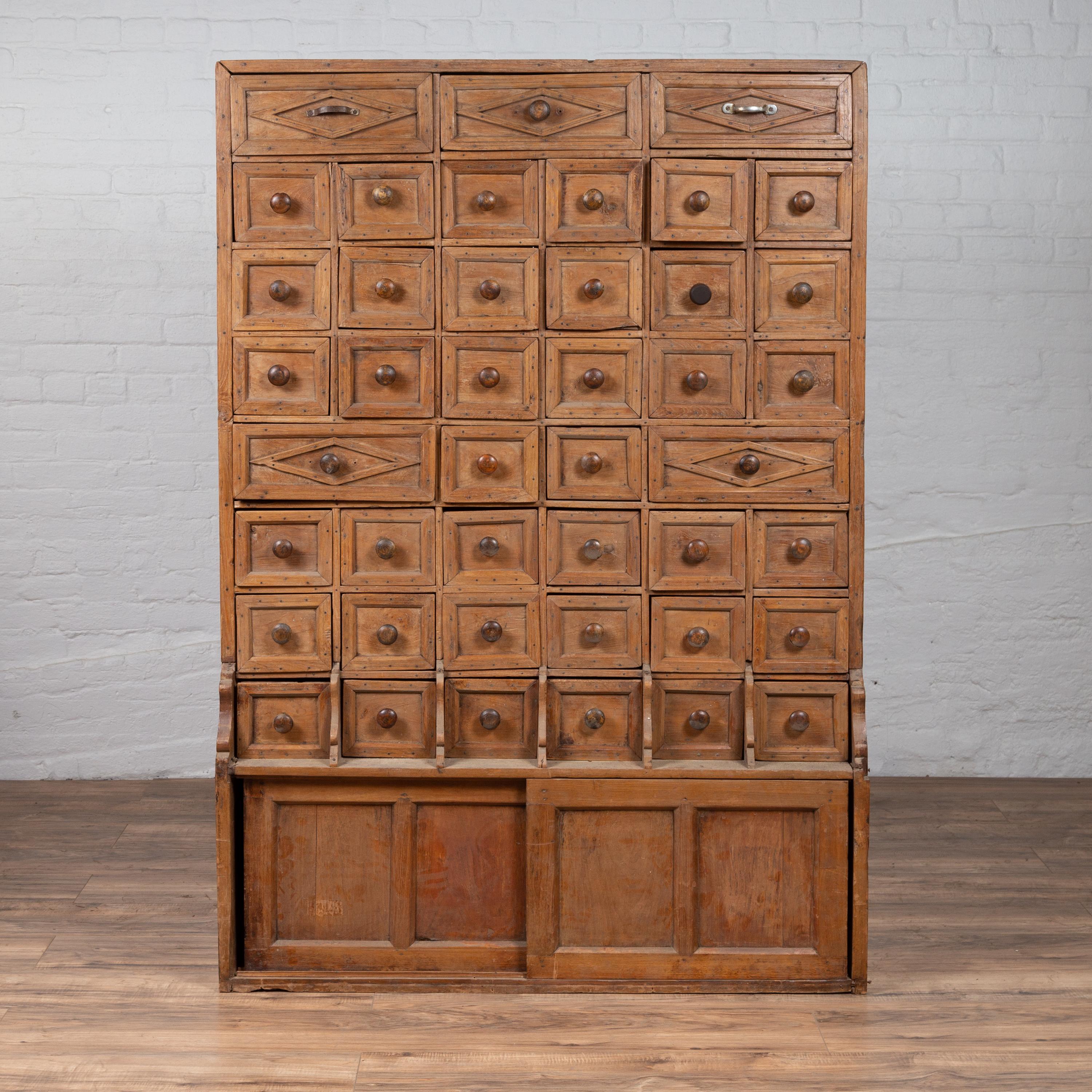 A rare Indian tall apothecary cabinet from the early 20th century, with multiple drawers and sliding doors. Born in India during the early years of the 20th century, this elegant apothecary cabinet features three drawers at the top, adorned with
