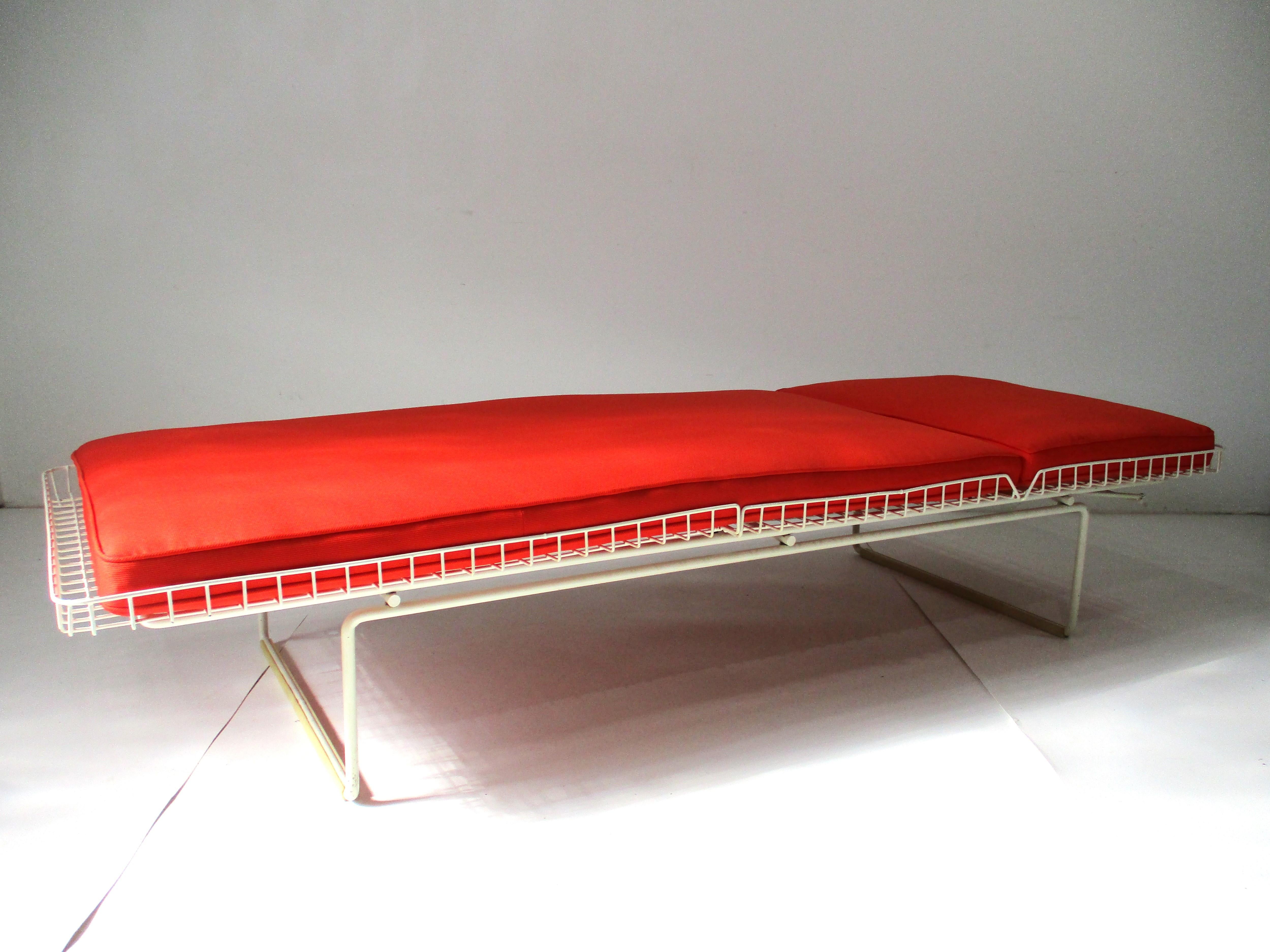 A white plastic coated wire chaise lounge with adjustable backrest and orange Knoll fabric two piece cushion . This rare chaise was produced for in door use since unlike the outdoor version does not have wheels . The piece has the original plastic