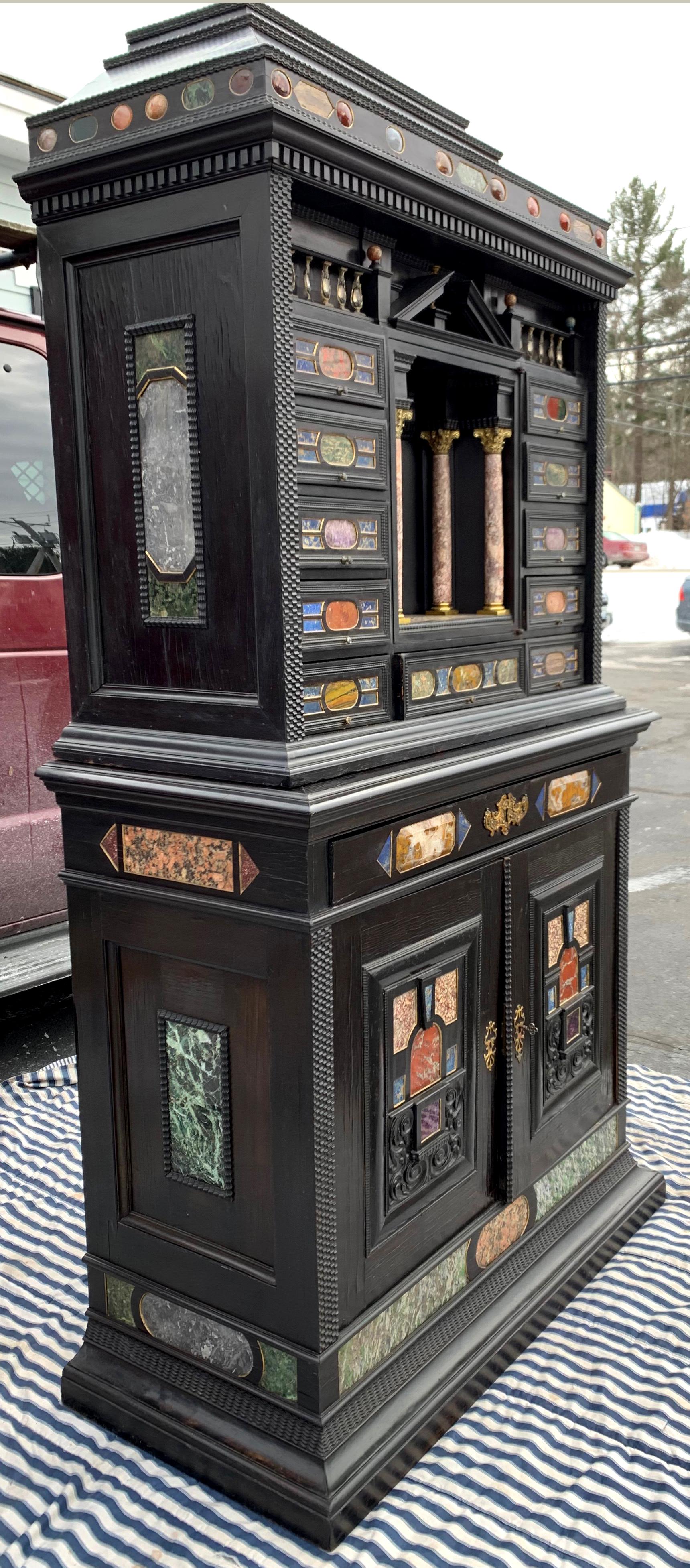 An exceptional two part rare Italian Baroque stone specimen collectors cabinet with ebonized finish, its upper case featuring a graduated stone decorated cornice surmounting a portico over a central door featuring a split pediment over four stone