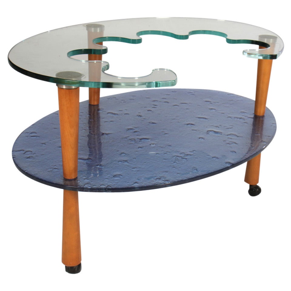A rare Italian two-tiered occasional table or bar cart having shaped glass top over blue cast glass lower shelf, supported by wood tapered and reverse tapered legs resting on casters.