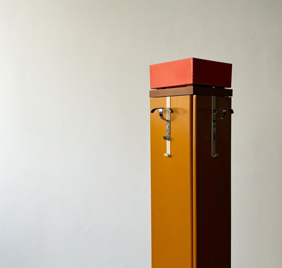 Dieser leuchtend senfgelbe Kleider- und Schirmständer aus den 1970er Jahren ist eine auffallende Mischung aus Funktionalität und Stil. Mit seinen vier Türen und Haken bietet es reichlich Platz für Mäntel, Hüte und Schirme, während der obere Teil des