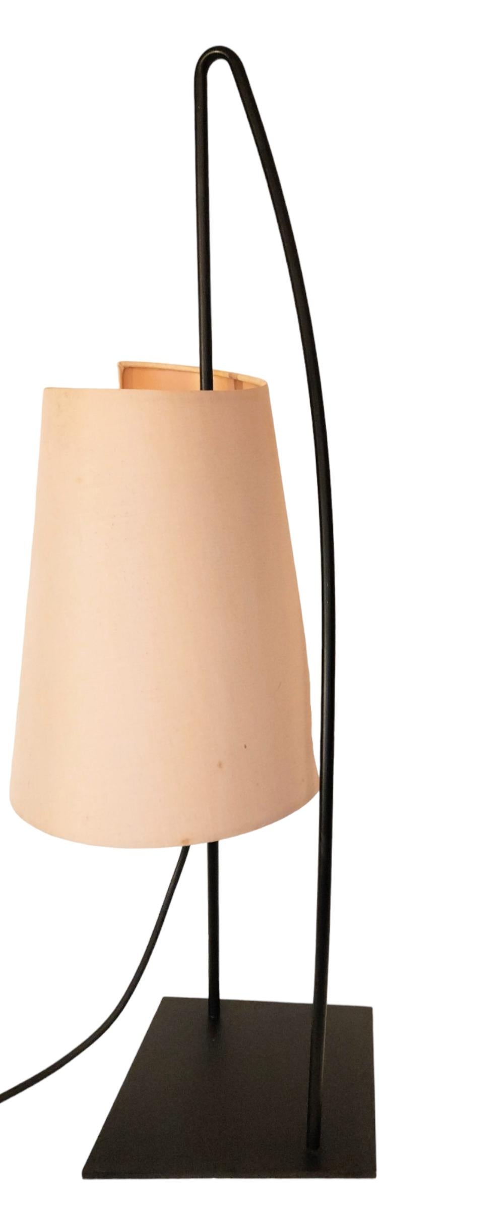 An Italian sculptural table lamp by Italiana Luce manufactured in Italy, circa 1960s.
The black lacquered base plate is slightly trapezoid. and supports a curved black lacquered metal loop.
The cast plastic socket slides up and down and rotates