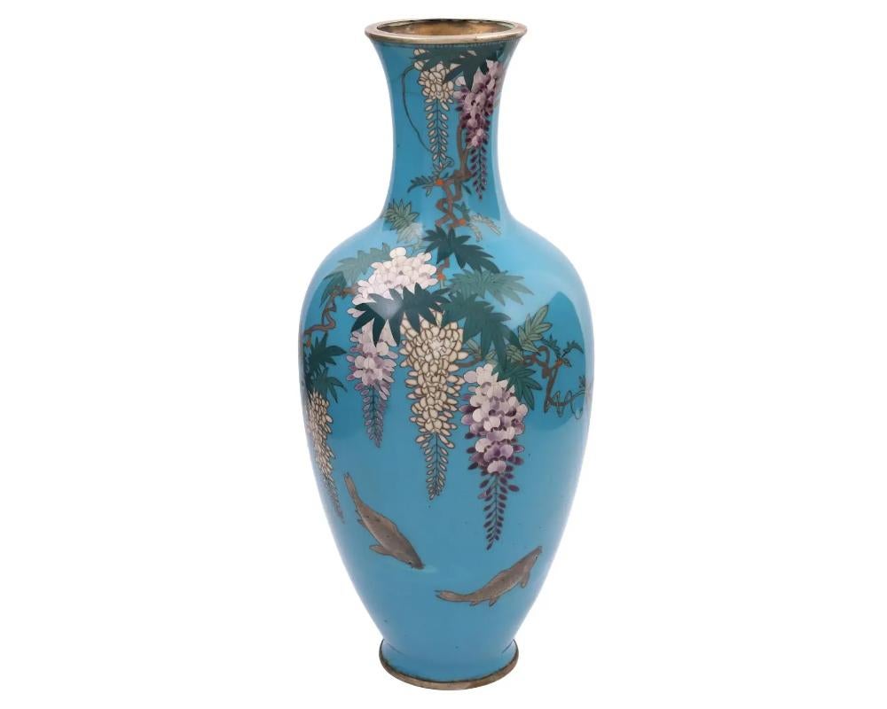 A rare antique Japanese, late Meiji period, enamel over copper vase.
The vase has an amphora shaped body and a long fluted neck.
The ware is enameled with a polychrome image of blossoming Wisteria flowers and fish on the turquoise ground made in the