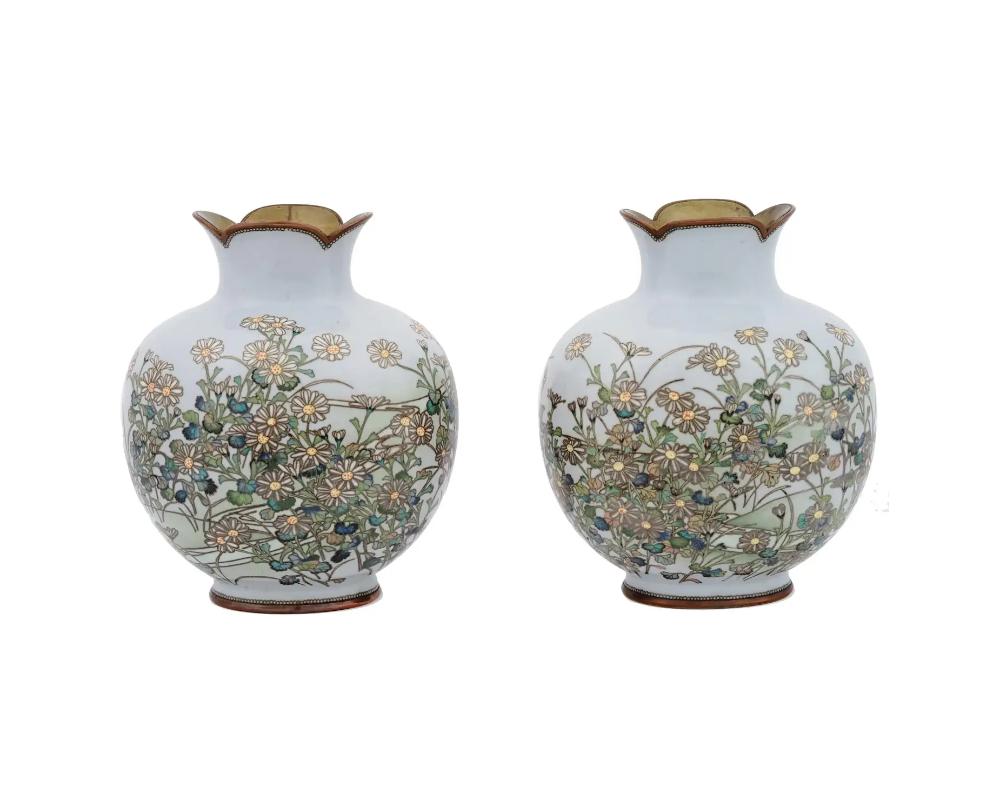 A pair of antique Japanese copper vases of flattened round shape with figurative rims. Late Meiji period, before 1912. The pieces are decorated with silver wire cloisonne enamel chamomile flowers against the light blue background. High quality.