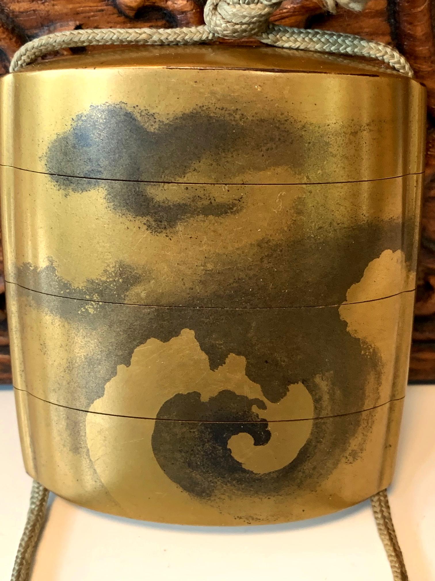 Ein dreiteiliger lackierter Inro der Familie Yamada aus der Edo-Periode (18.-19. Jahrhundert). Das Inro mit leicht gerundeter Form ist im Kano-Stil gehalten und stellt einen Drachen dar, der zwischen Tintenwolken auf einem goldenen Hintergrund
