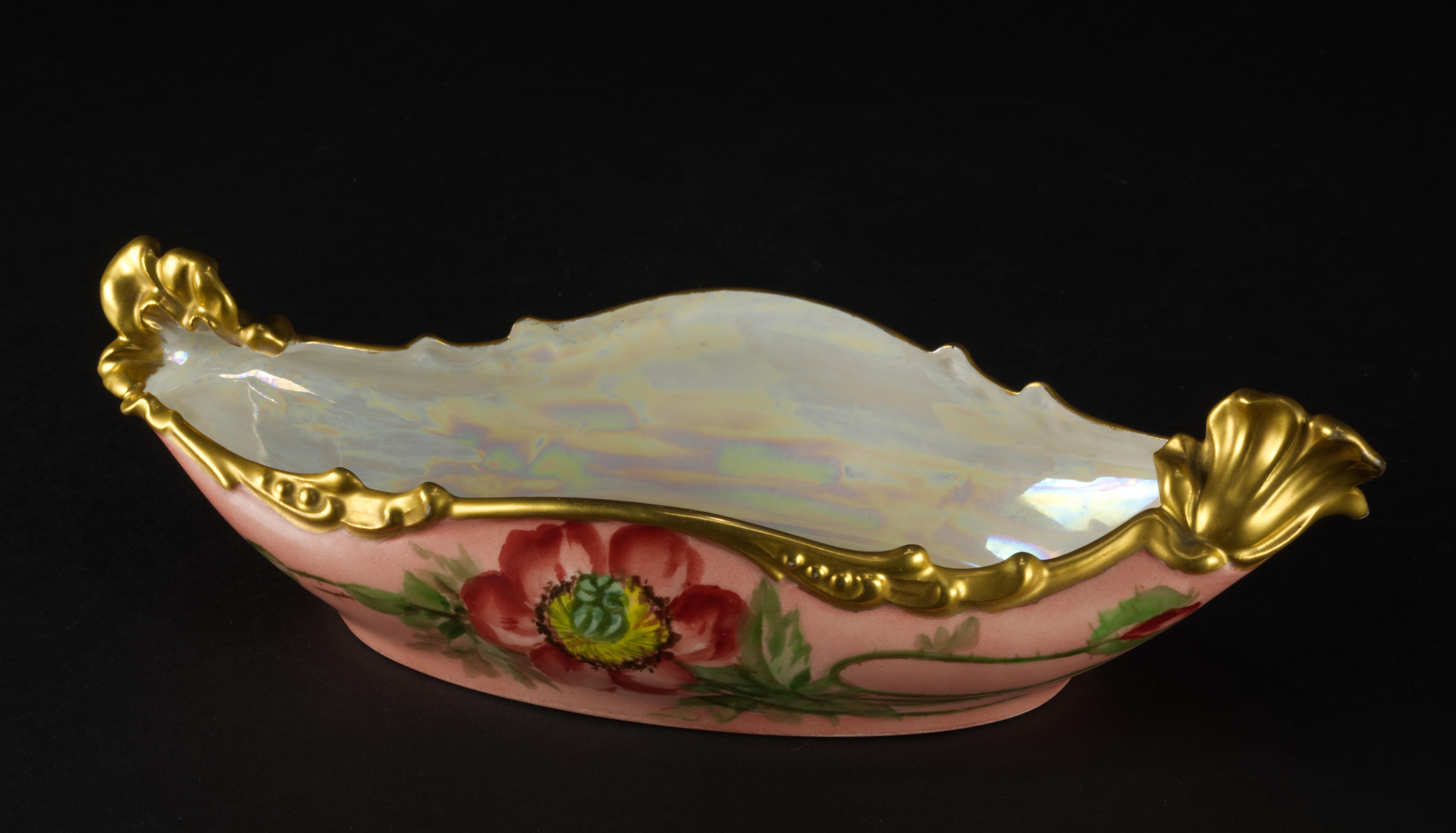 
Rare Jean Pouyat porcelain ravier plate or serving bowl is hand painted with red poppy flowers on pink background and decorated with elaborate Art Nouveau style gilded trim; wavy, organically shaped rim flows around the bowl with two raised areas