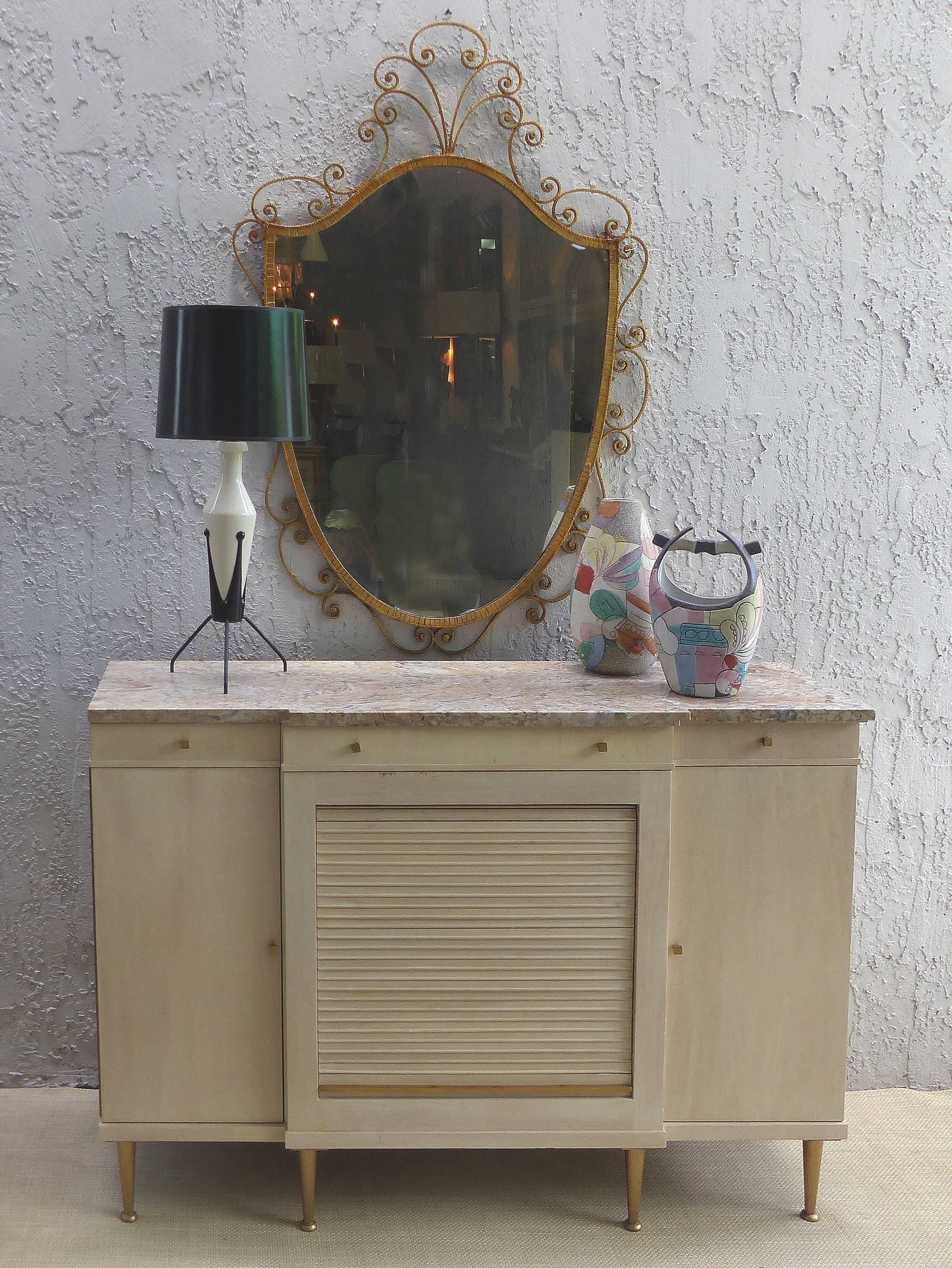 Offered for sale is an elegant 1940s Hollywood Regency marble topped credenza by John Widdicomb. The shallow cabinet has a colored marble top with brass hardware and legs; it is finished in a light washed cream color. The centre has a tambour door