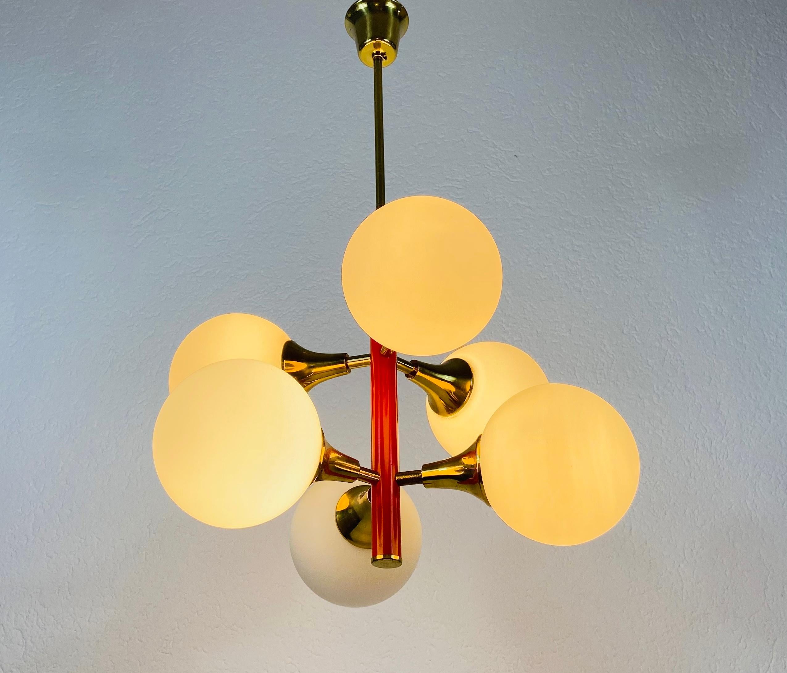A midcentury chandelier by Kaiser made in Germany in the 1960s. It is fascinating with its Space Age design and six opaque balls. The red circular body of the light is made of full metal, including the arms. Brass bar with brass canopy.


The