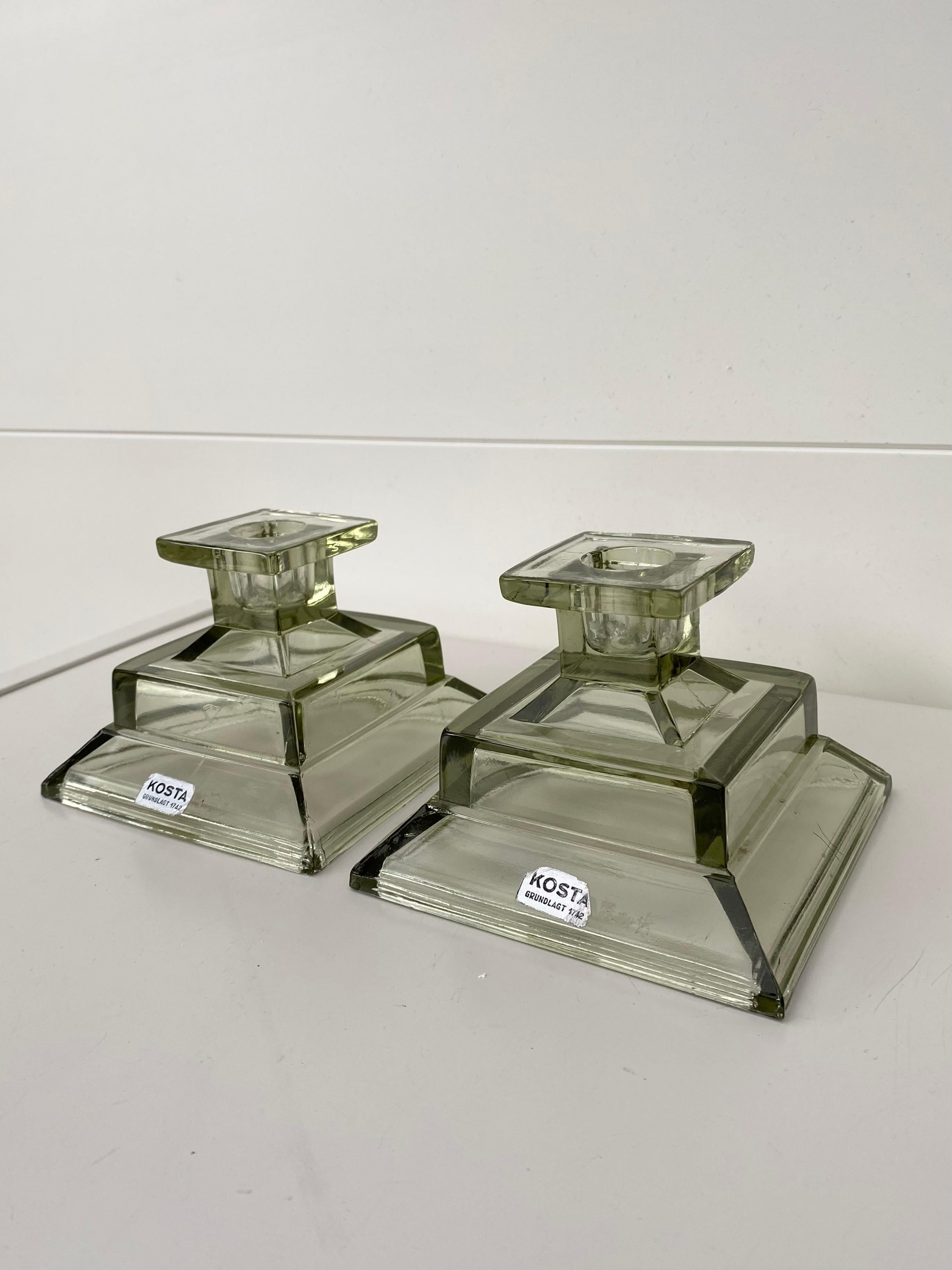 Pair of two smoked Glass candlesticks, manufactured by Kosta Glasbruk which was founded in 1742 and later became Kosta Boda Sweden. Signed with a sticker ‘Kosta Grundlagt 1742’. Appearance greenish / grayish. Remain in Good condition with wear