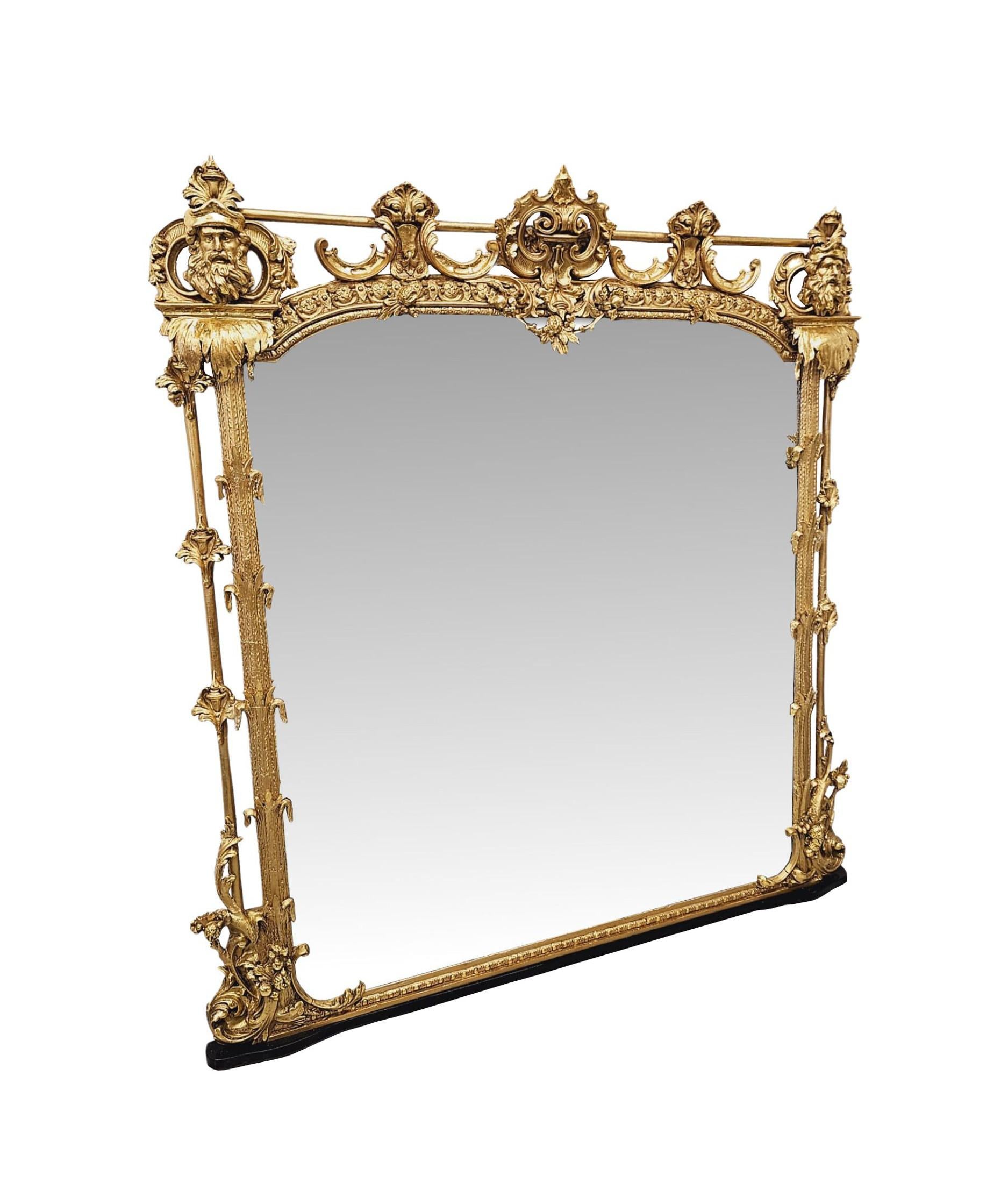 A very rare 19th Century castle or country house giltwood overmantel mirror of exceptional quality and grand proportions featuring Neoclassical motifs throughout.  The shaped mirror glass plate of rectangular form is set within a finely hand carved