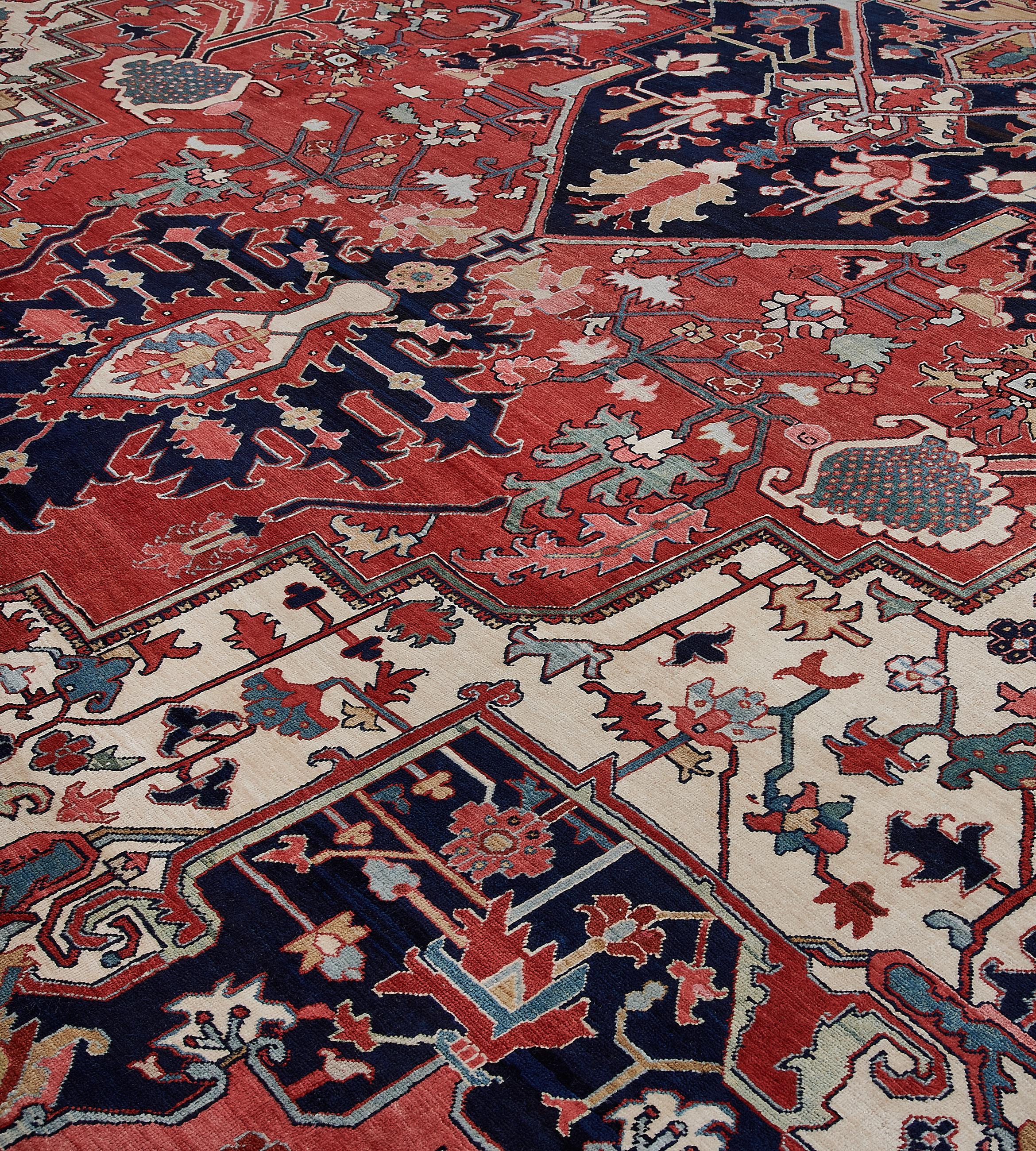 This traditional hand-woven Persian Serapi rug has a brick red field of whimsical geometric floral sprays enclosing a deep indigo and beige imperial medallion and in soft ivory spandrels of similar geometry, in a deep indigo linkedserrated leaf