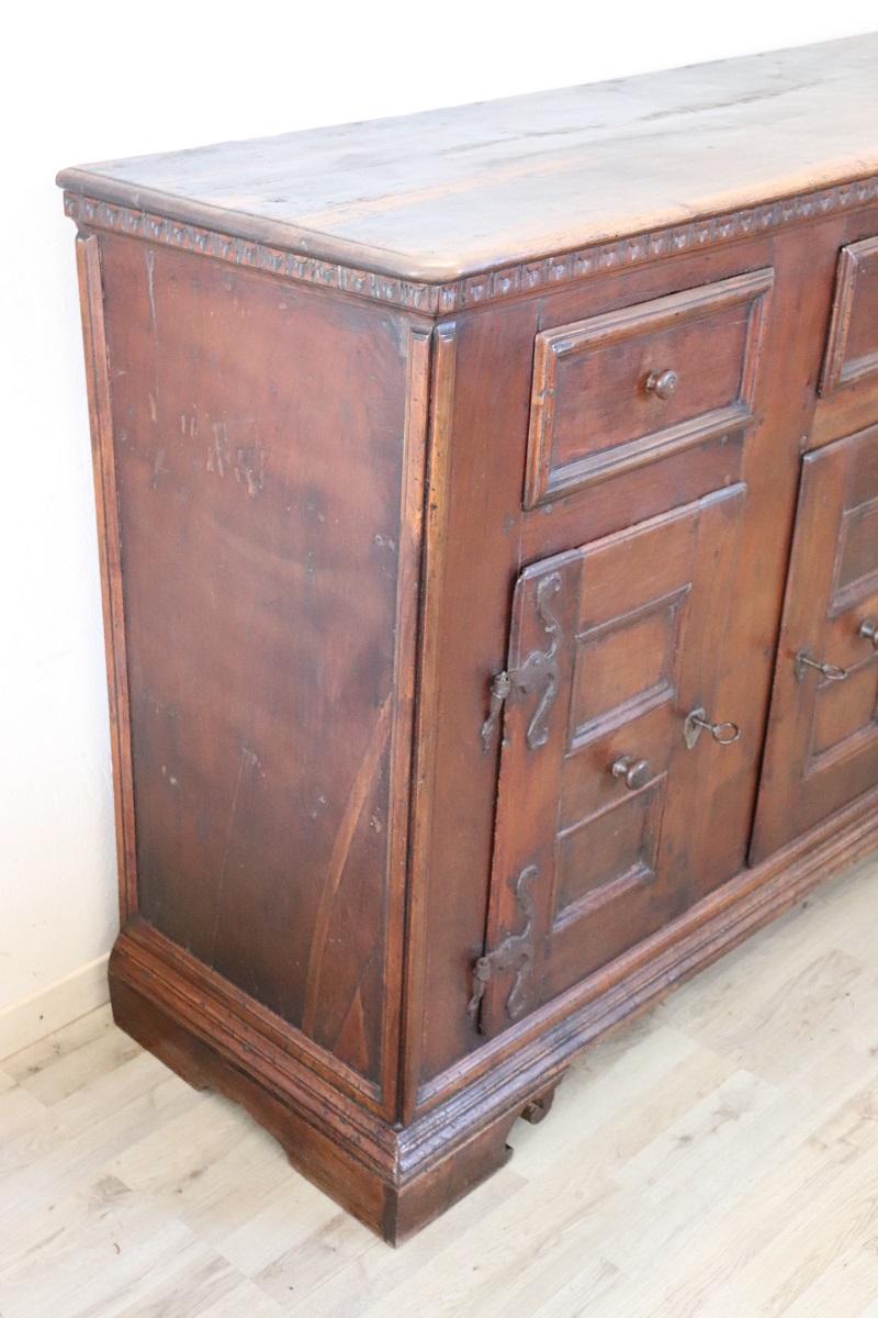 Gregorius 17th century Italian Louis XIV solid walnut wood antique sideboard. Equipped with three comfortable drawers and three beautiful doors. Beautiful large iron hinges can be seen on the doors. Presence of ancient restorations which have not