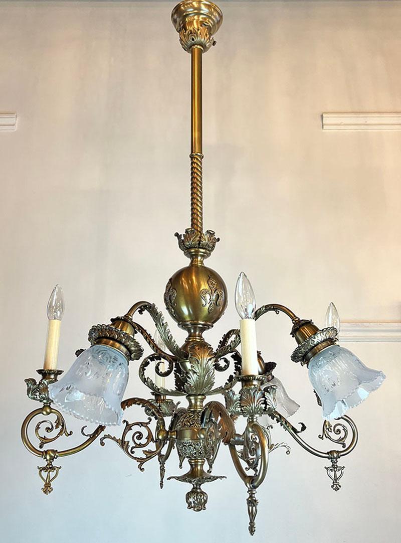 What a fixture! Very high end in its day, this 8 light combination chandelier was originally gas and electric. Features rich fine acanthus and floral castings as well as a Fleur de lis motif on the center body. Fleur de lis stencil etched shades are