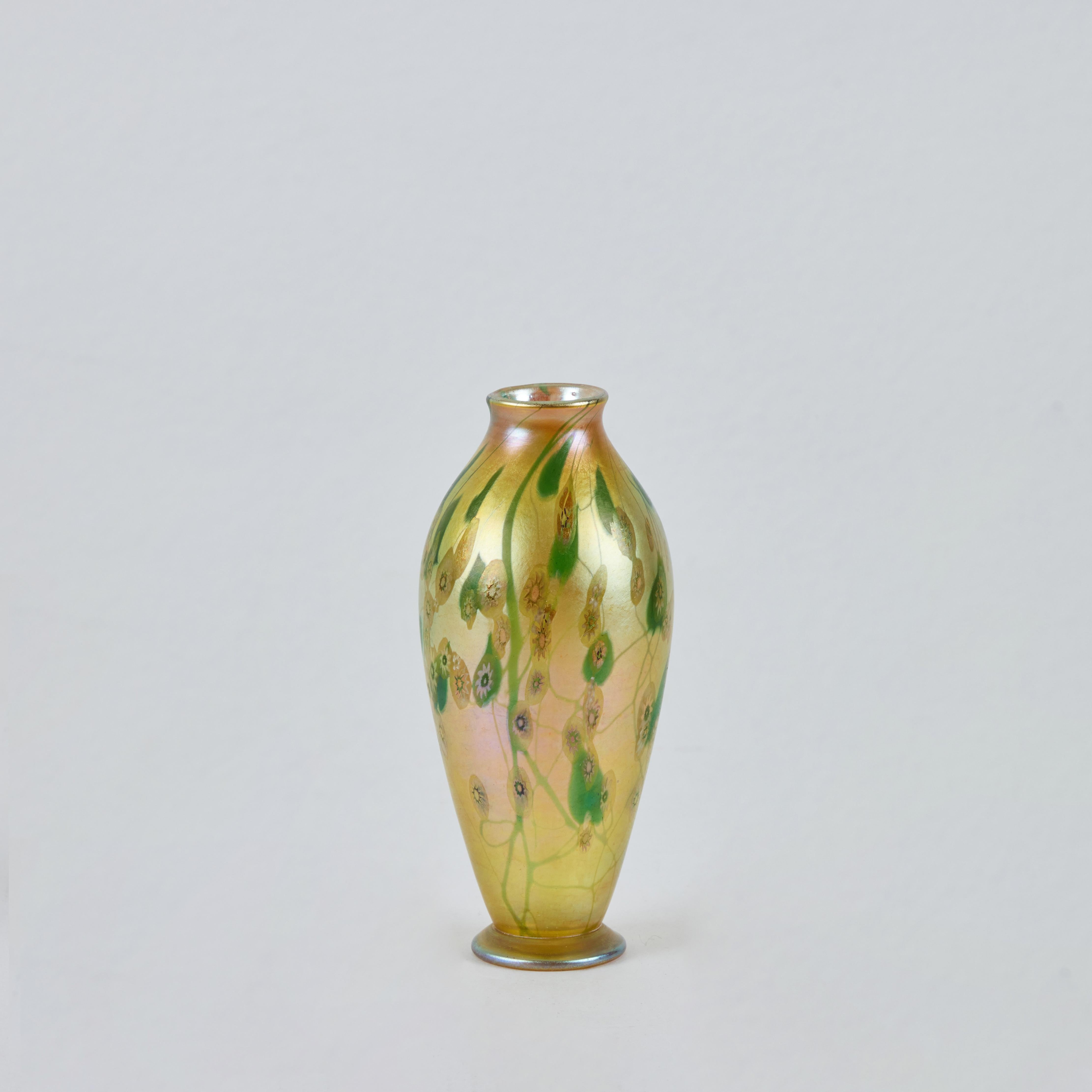 Questo vaso in vetro Favrile, luminoso ed eccezionale esempio della maestria di Louis Comfort Tiffany, risale al 1900 circa. Il vaso presenta una graziosa forma a balaustro allungata con un bordo dolcemente svasato e una base con piedi. La sua