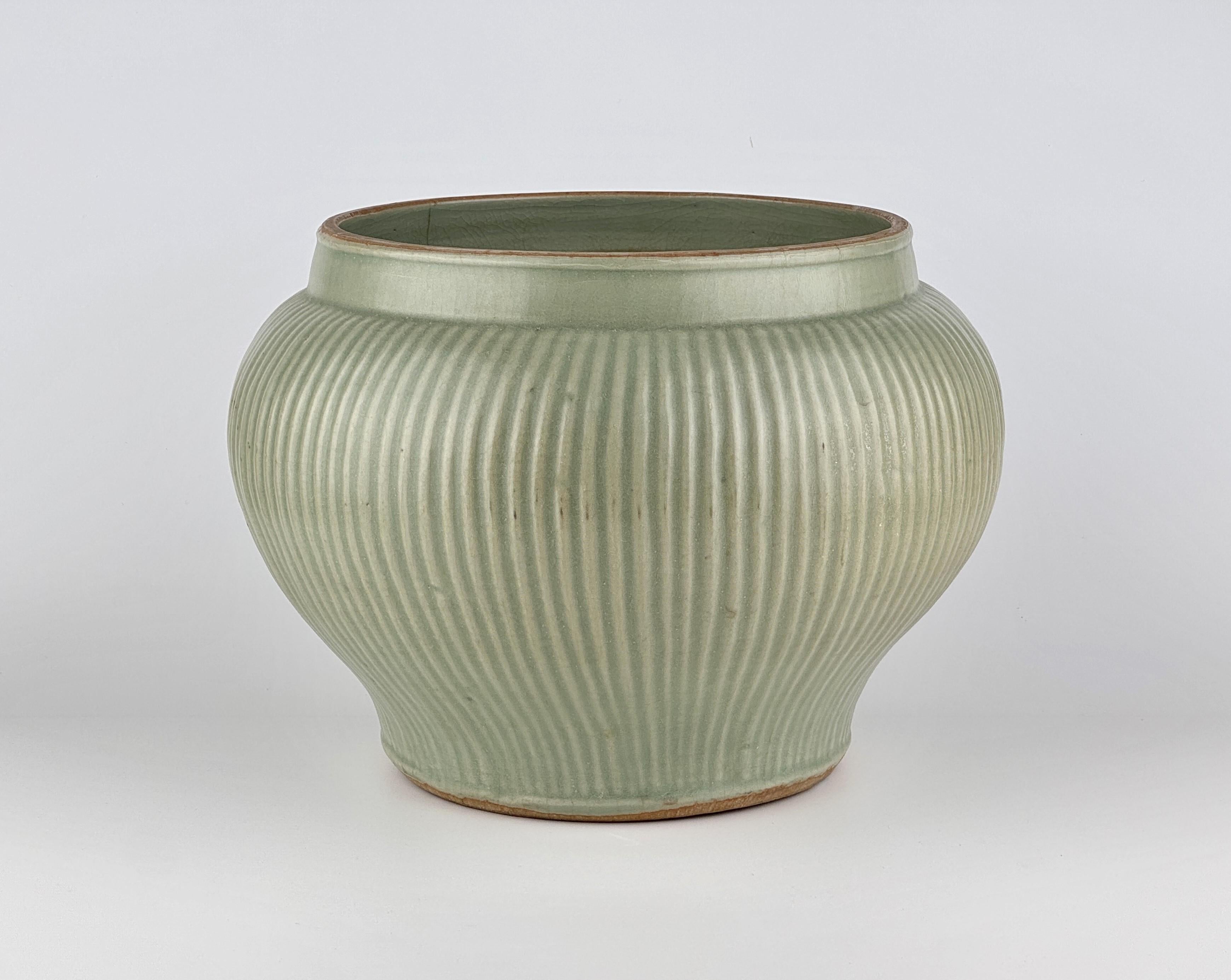 This beautifully crafted jar features a wide baluster form, swelling gracefully from a short and slightly tapered foot. The design is accentuated by slender, elegant vertical ribs throughout. The glaze exhibits a subdued luster, reflecting the