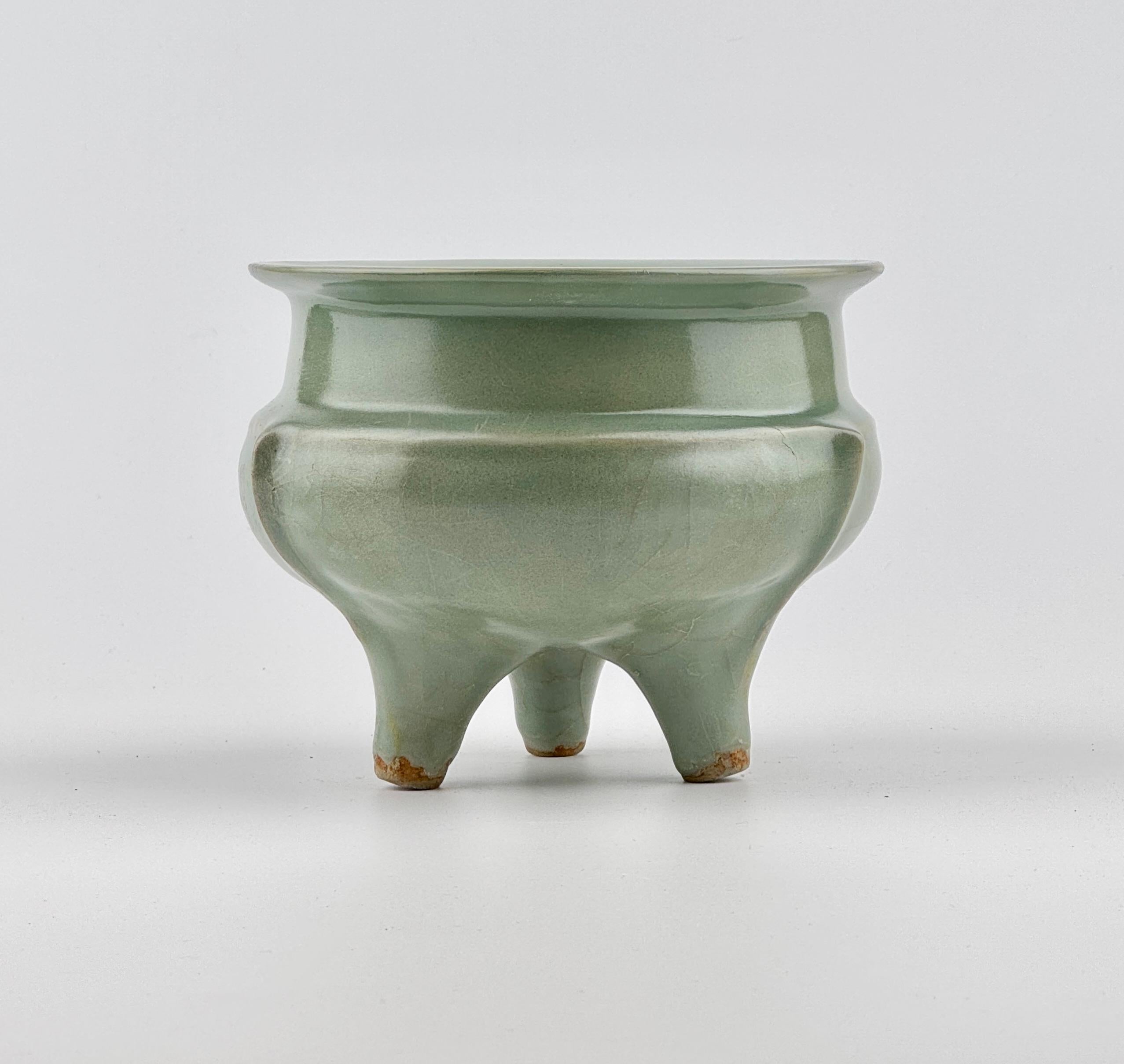 The vessel features a compressed body supported by three tapered feet and a flat, outwardly flaring rim. Three slender flanges originate from a subtle ridge on the shoulder and extend gracefully down each leg. The entire censer is adorned with a