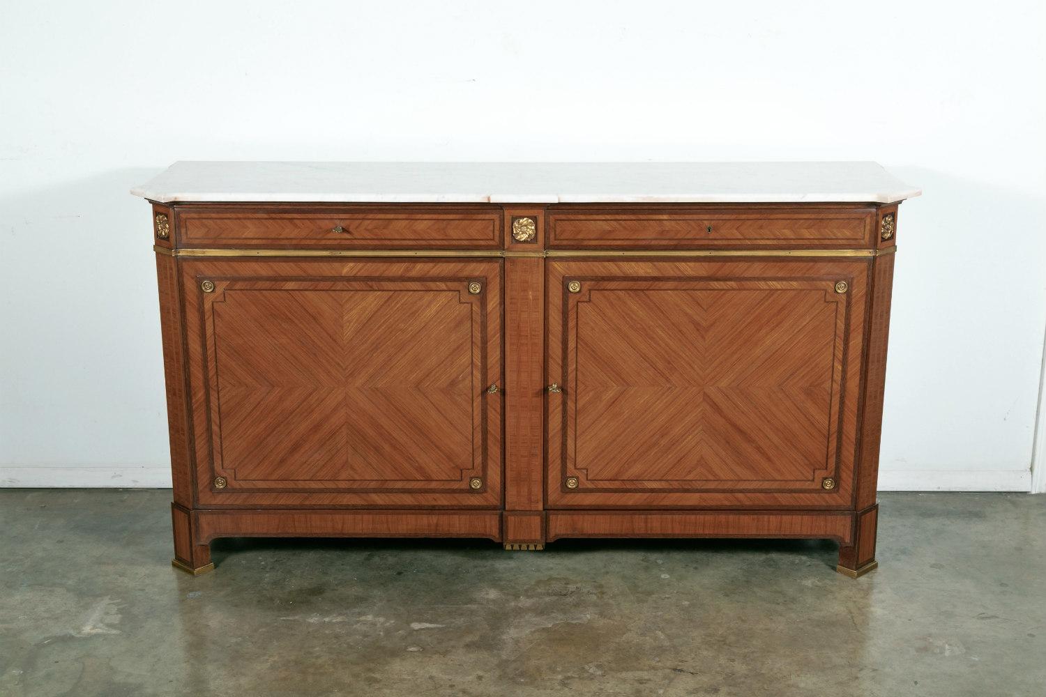 A rare and extremely elegant French Louis XVI style inlaid parquetry and marquetry buffet by Maison Gouffé, Paris, having a shaped Carrara marble top with projecting canted corners and finely chased bronze ormolu mounts and brass trim. This stunning