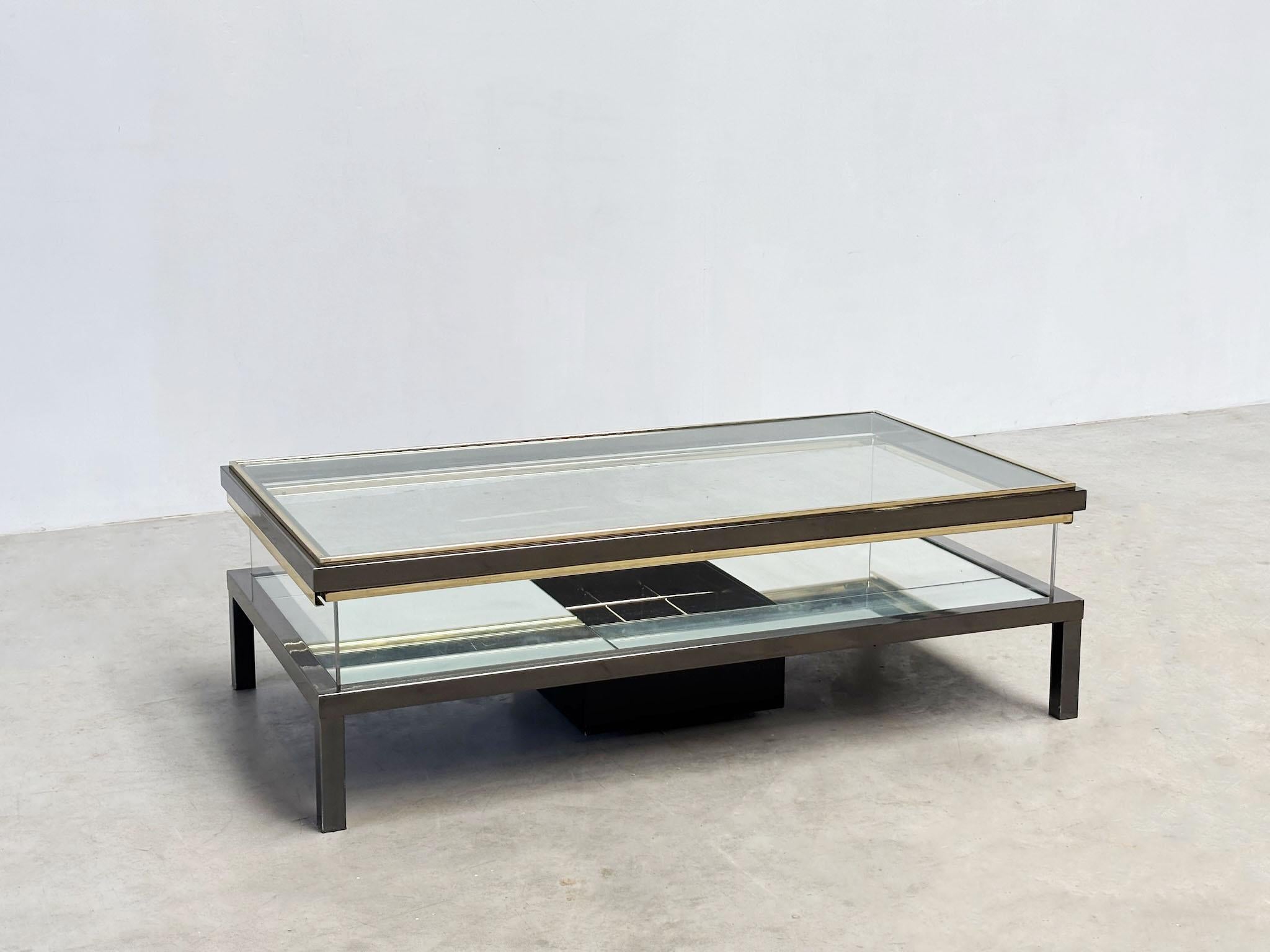 This stunning 1970s French coffee table is likely a creation of the renowned design house Maison Jansen. It features a unique sliding glass top that reveals a display compartment with a bottle holder. Crafted with a brass trim and sturdy steel