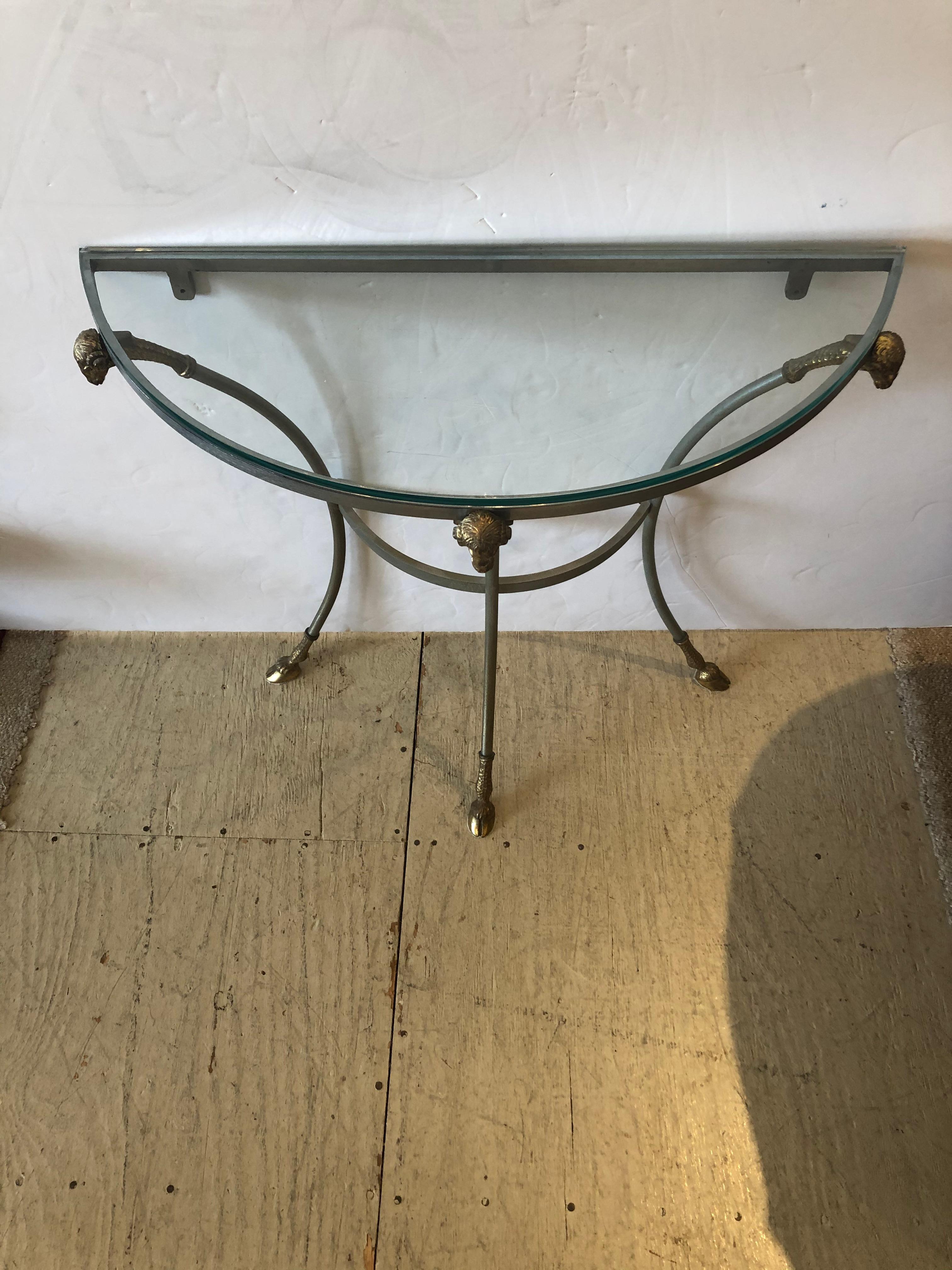 A very rare elegant demilune console table having sleek steel base adorned with 3 brass rams head at the top and hoof feet. New piece of glass.
