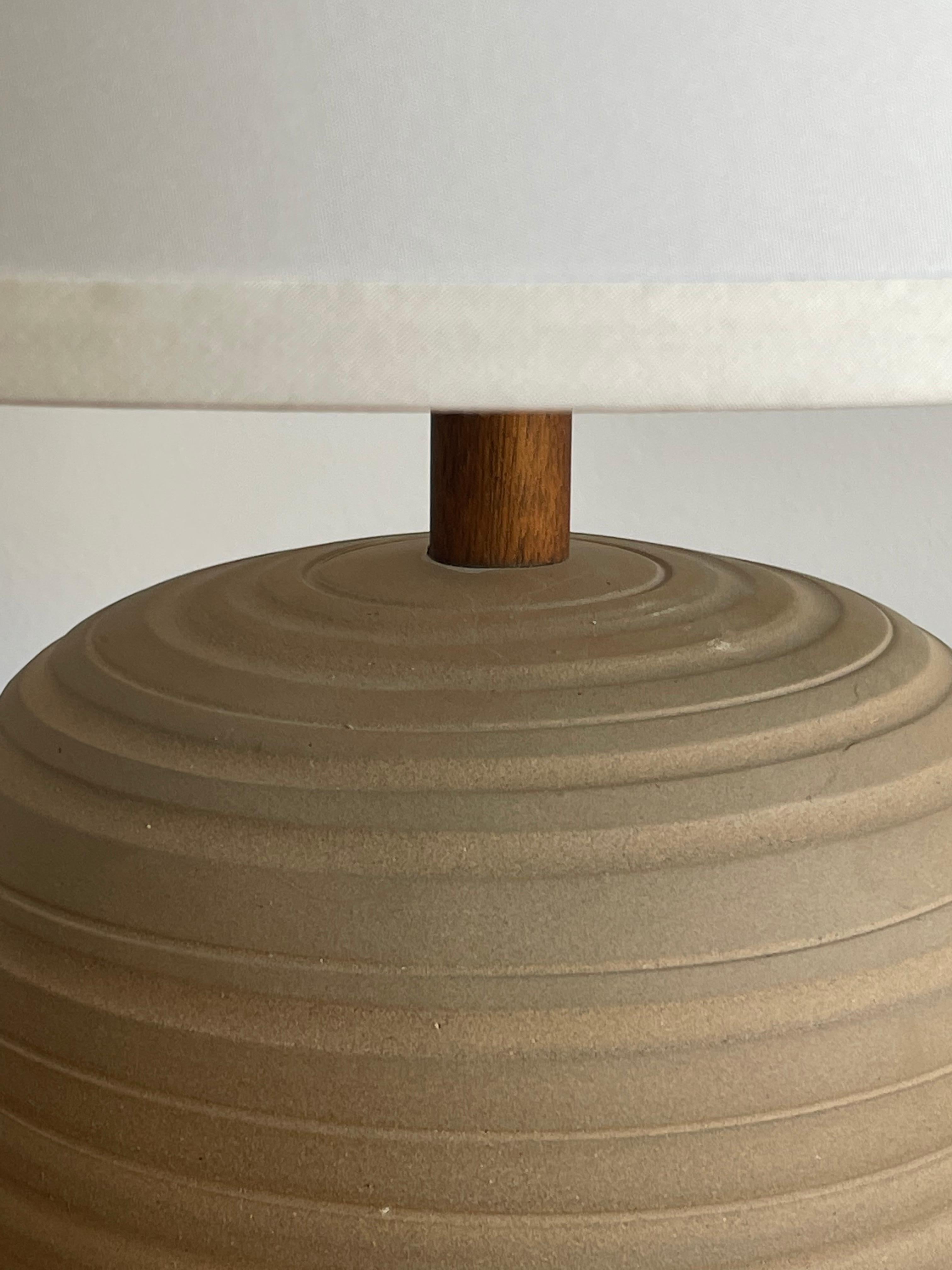 Unusual ceramic table lamp by famed ceramicist duo Jane and Gordon Martz for Marshall Studios. Features a seemingly unglazed but incised body, creating a very natural color palette. Accented with walnut neck and finial.

Measures: 
Overall