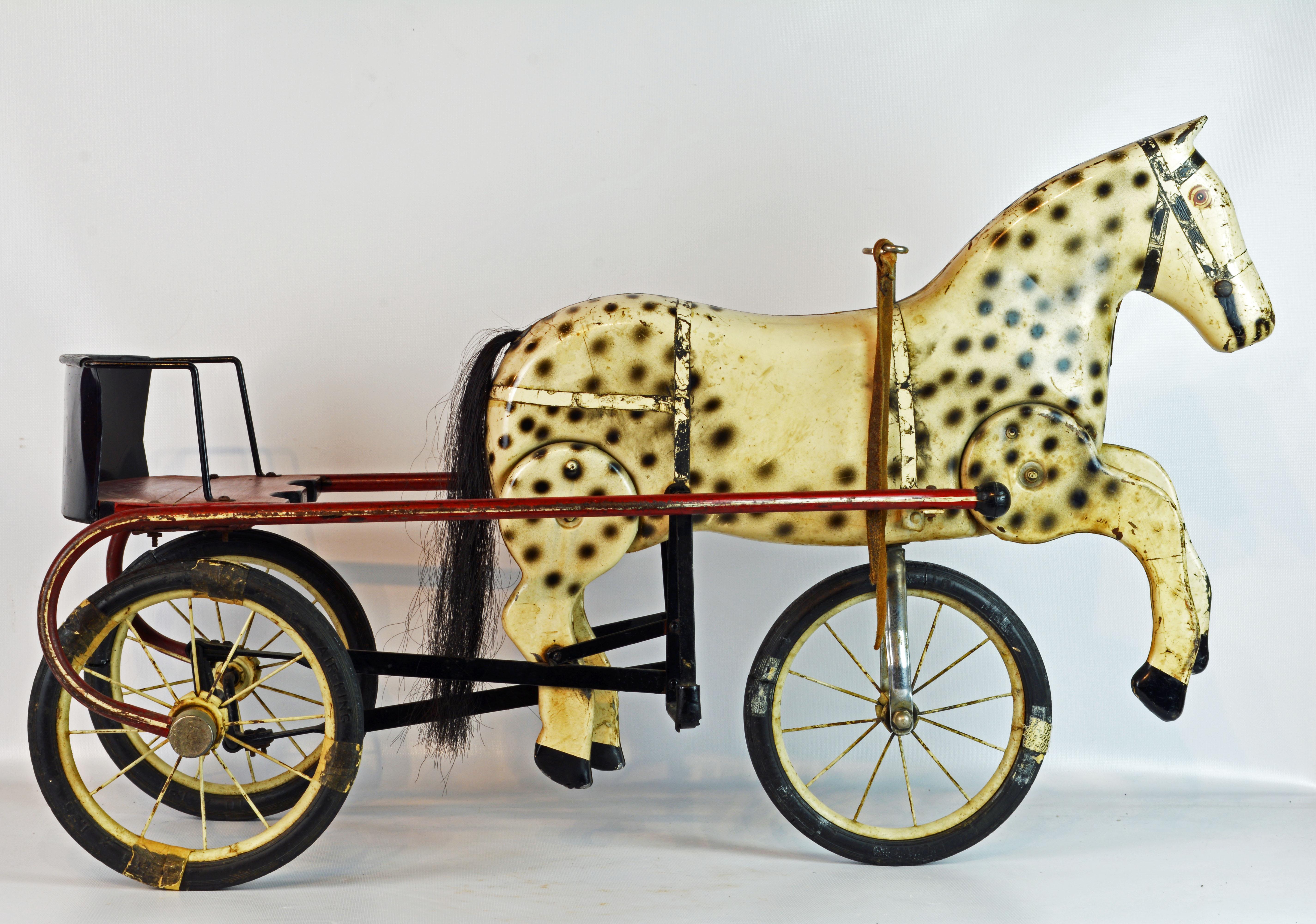 This sulky style pedal tricycle features a seat supported by two wheels and an intriguing tole horse mounted on the front wheel in a way that lets the horse legs move as the tricycle moves forward.