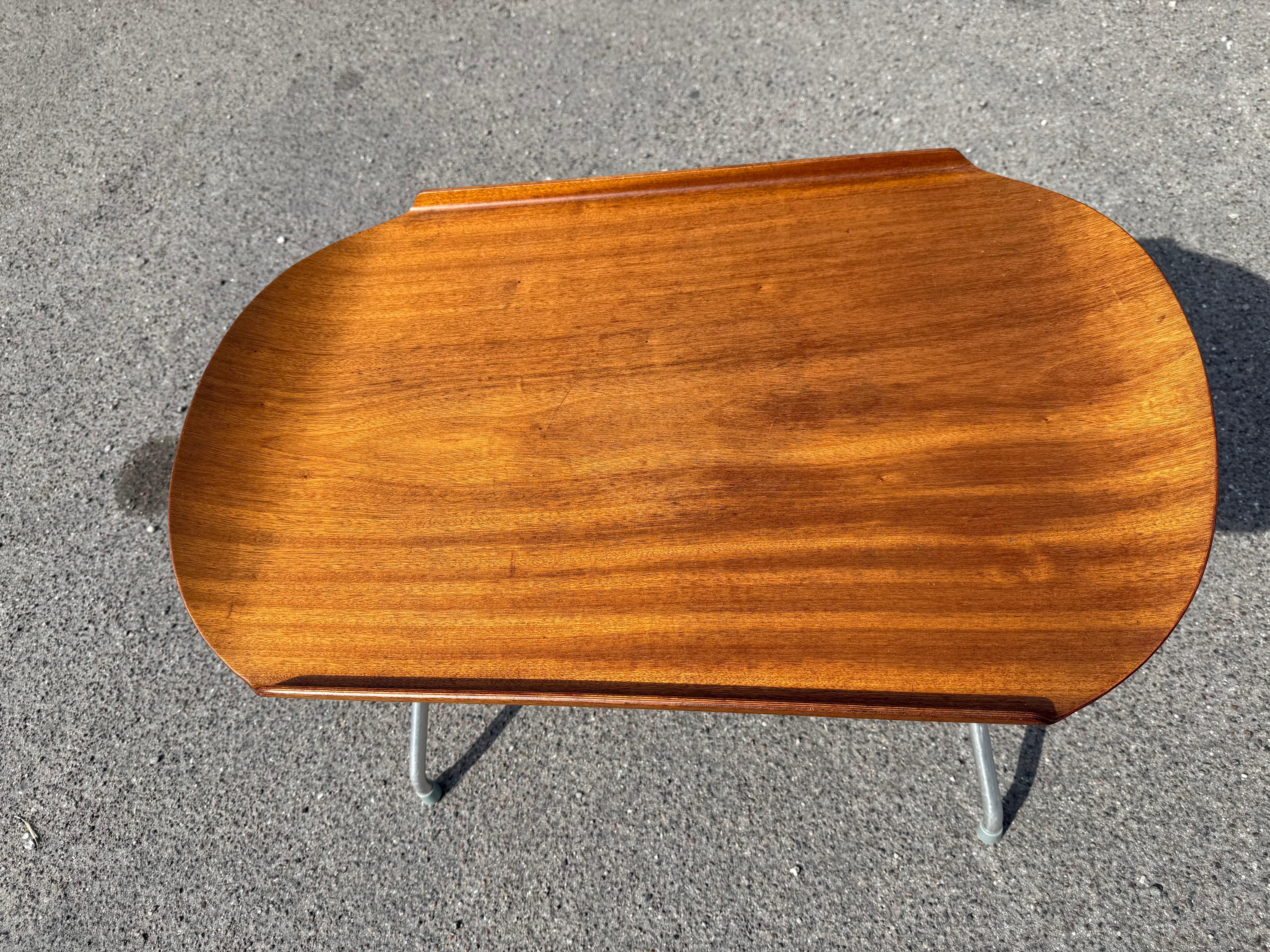 This Mid-Century Norwegian Alminette Teak Folding Tray Table by f.m. Produkt, Frederiksberg Metalvarefabrik from the 1960s exemplifies elegant design and practicality. Comprising two main elements—the teak-shaped wood tabletop and the metal