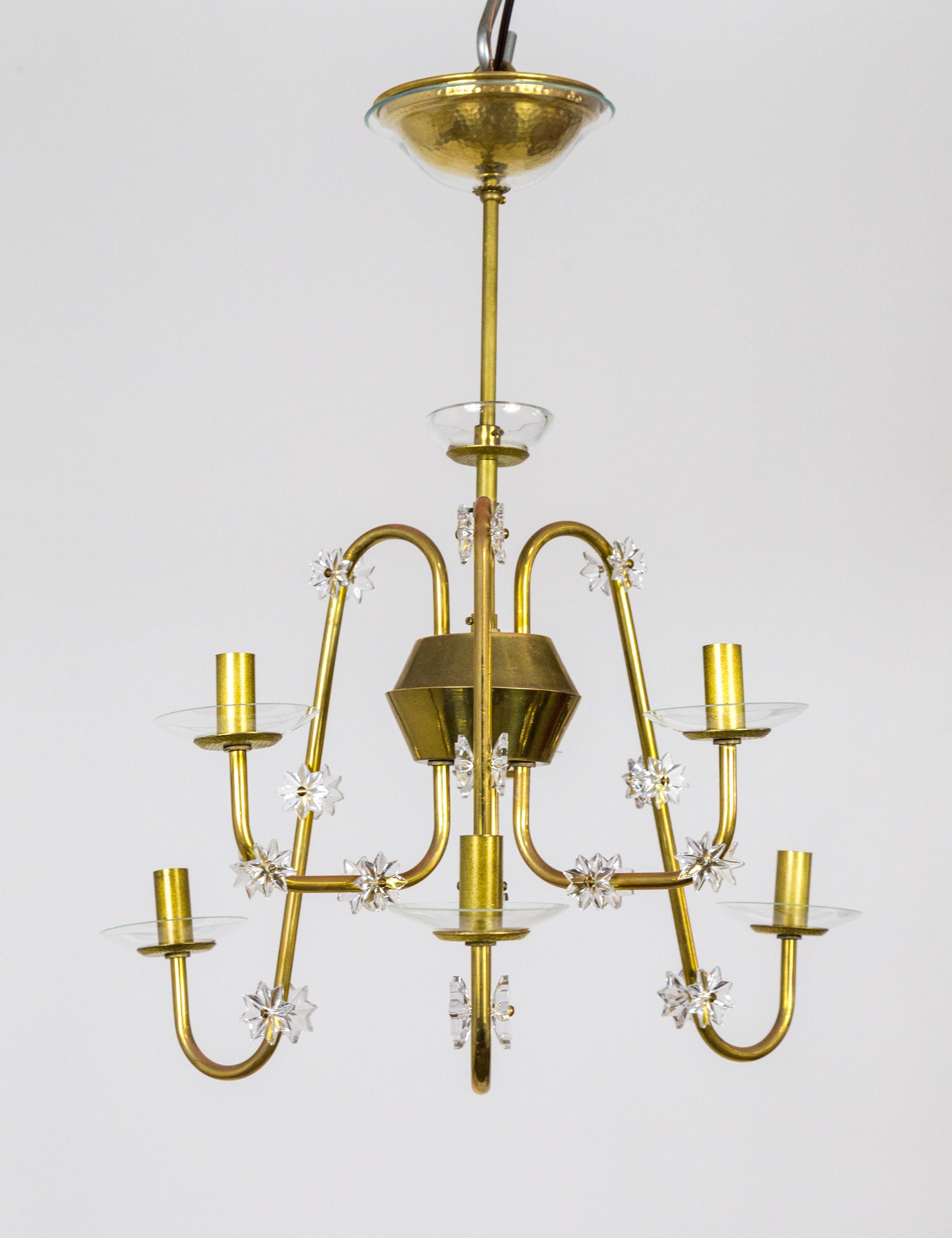 A streamlined, Mid-Century Modern, brass chandelier with six arms swooping up and down from the main stem piece. Delicate, glass bobeches sit on hammer-textured brass disks, echoed on the mid point of the stem. With a glass covered canopy and star