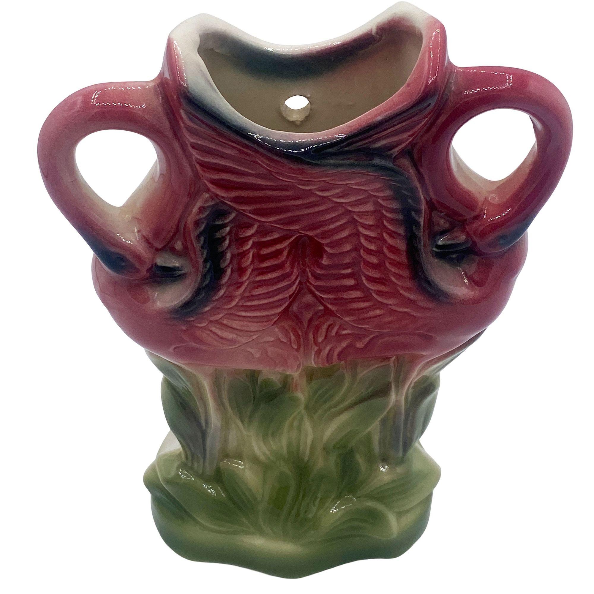 Mid-century pink and green ceramic flamingo California pottery flower wall vase. The wall vase features a beautifully detailed pink flamingo pair locking together on a lush green grassy field. It comes in a gloss finish that highlights the rich