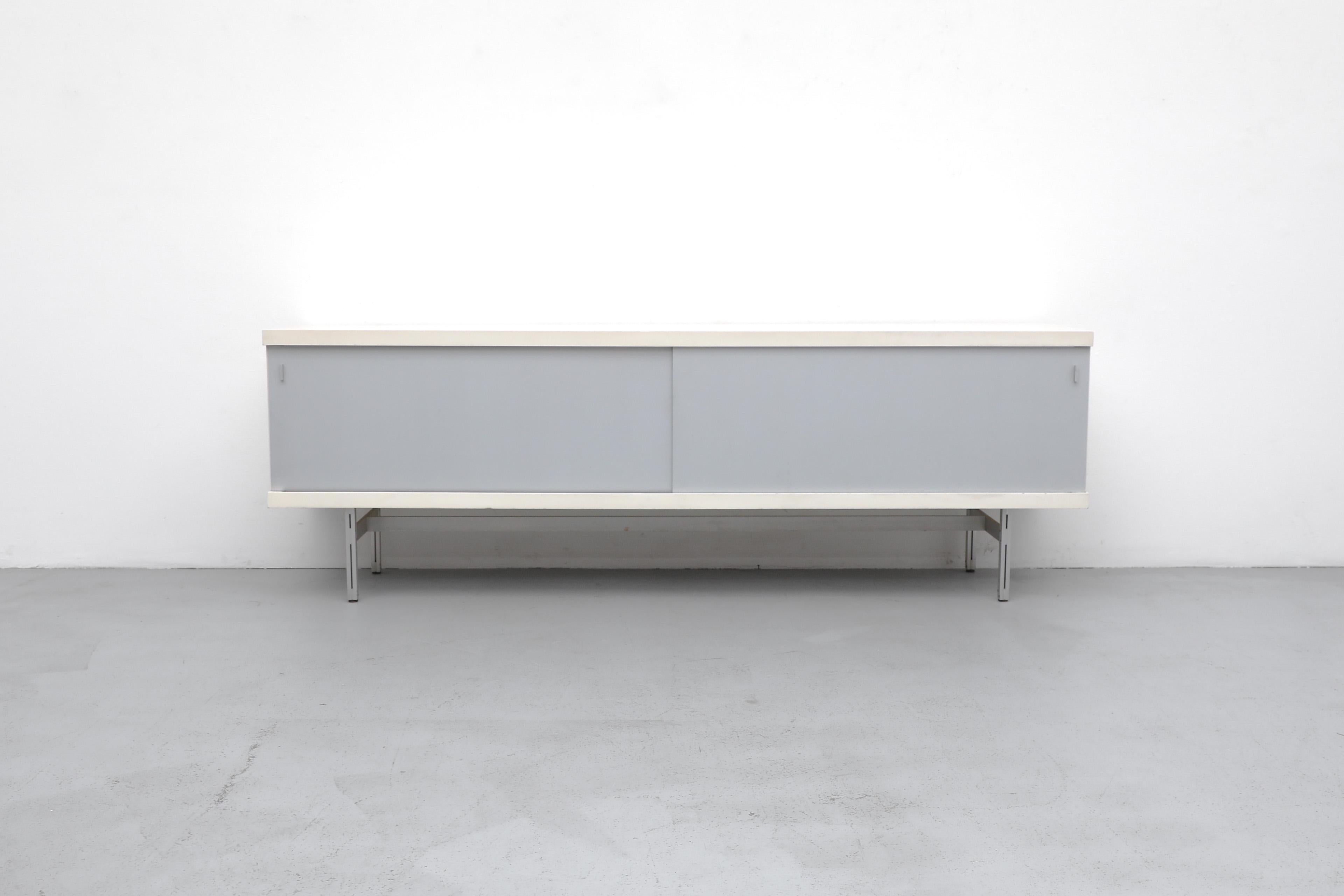 Ce rare buffet de l'édition des années 1960 de Horst Brüning pour Behr Germany repose sur un cadre en aluminium avec un corps laqué blanc cassé. Les portes coulissantes en aluminium lourd dissimulent 2 compartiments d'étagères et un ensemble de
