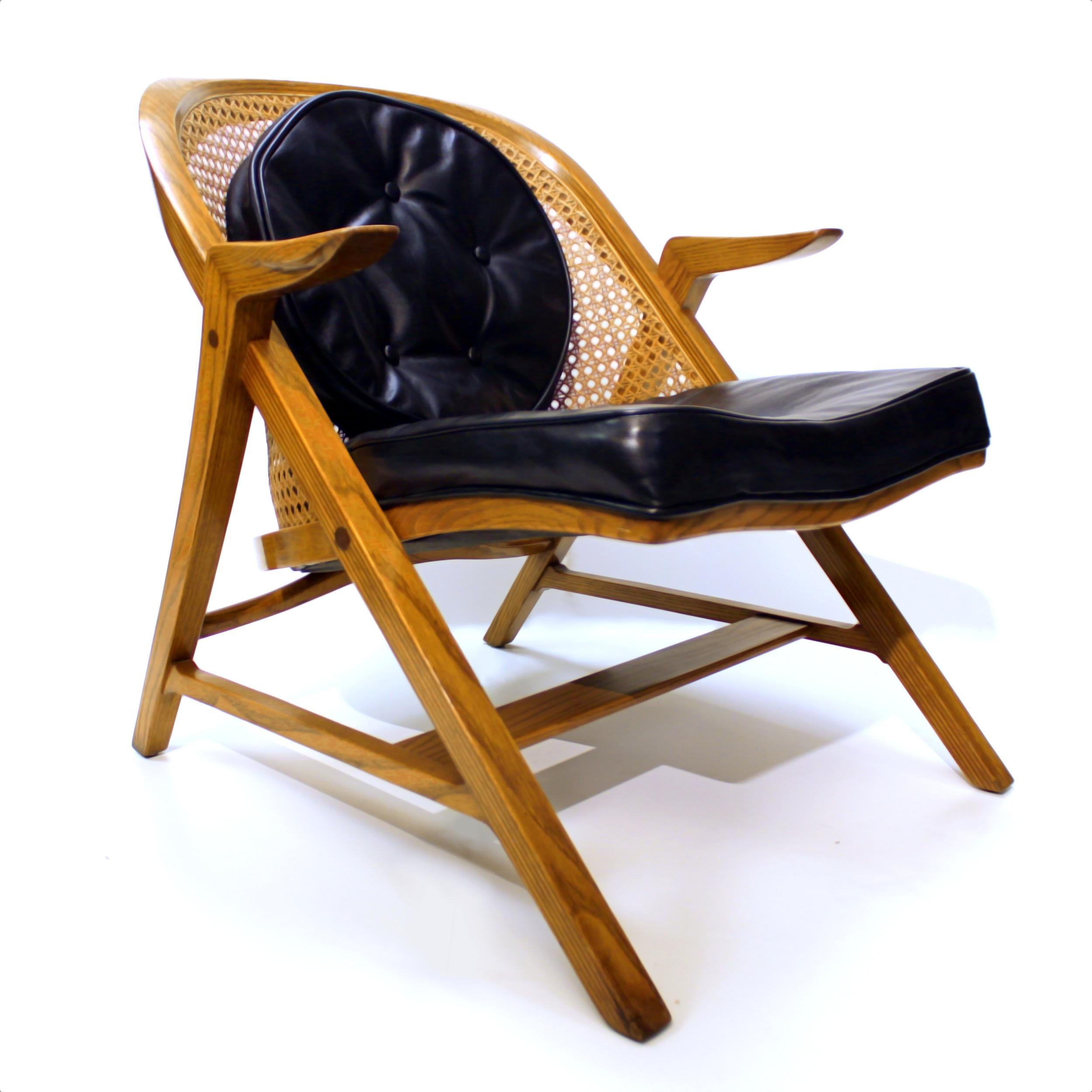 Wonderful 5700-A lounge chair designed by the renowned Edward Wormley for the Dunbar Furniture Co. This rare chair features a beautifully sculpted oak frame, cane barrel back, and black tufted leather seat and pillow. An exceptional example of an