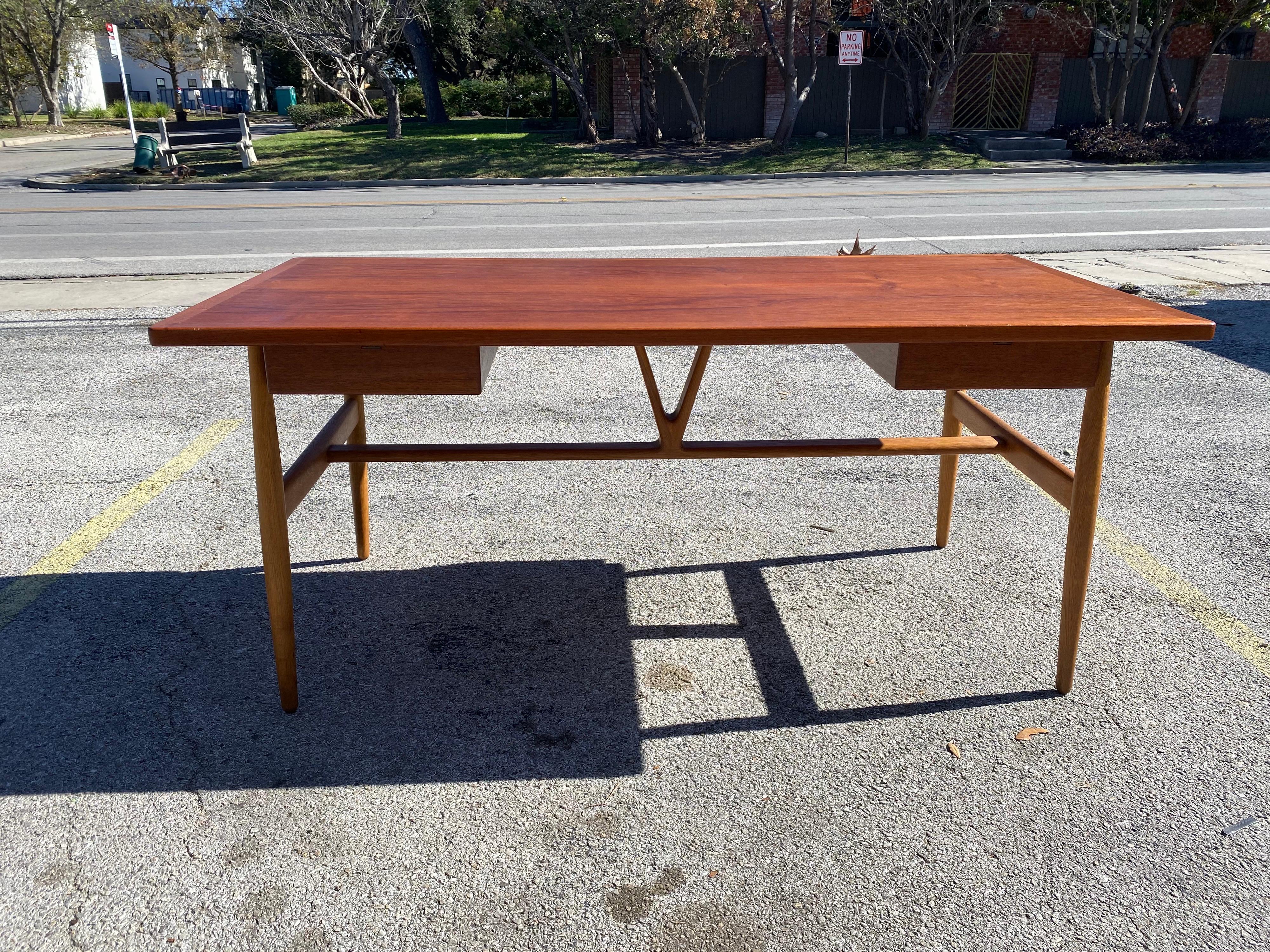 Rare mid-century modern JH-563 Wishbone desk by Hans J. Wegner produced by Johannes Hansen, circa 1950s, Denmark. This beautiful mid-century desk features a teak top, two drawers with sculpted handles, and a solid oak frame with a stretched