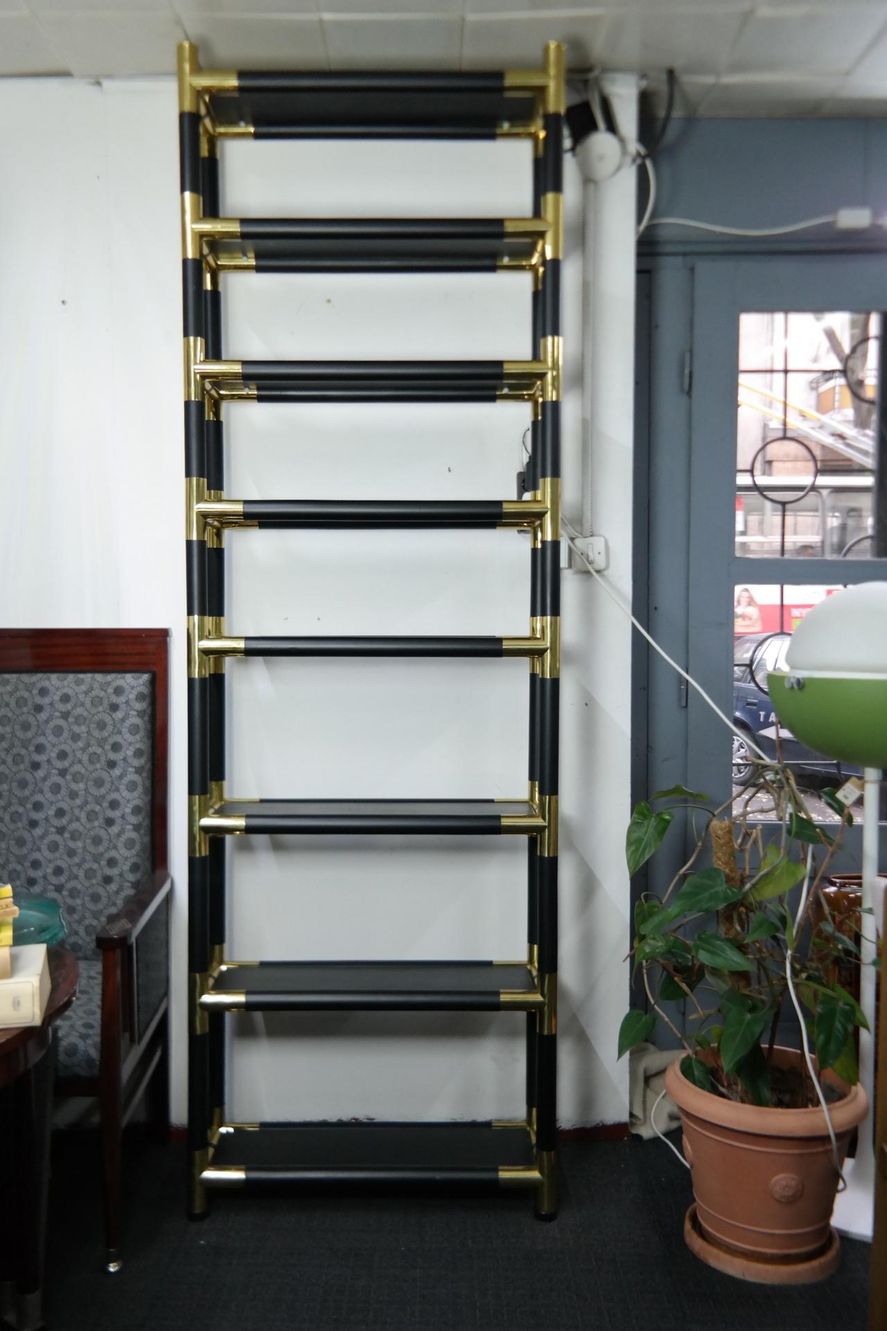 This tall bookshelf features wooden shelves and massive brass joints. It's a rare Mid-Century Modern piece from the 1970s.
  