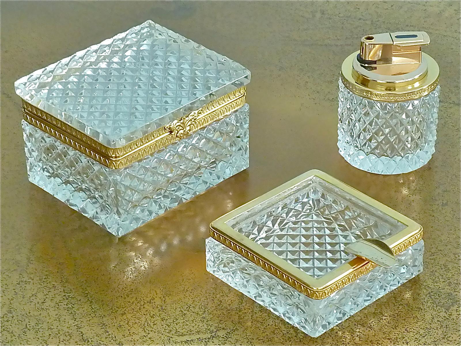 Gorgeous mid-century hand-cut and faceted crystal glass smoking set with decorative gilt brass metal rim made by Baccarat France attribution, circa 1950-1960. The exquisite french set which comprises one ashtray, one table lighter and one cigarette