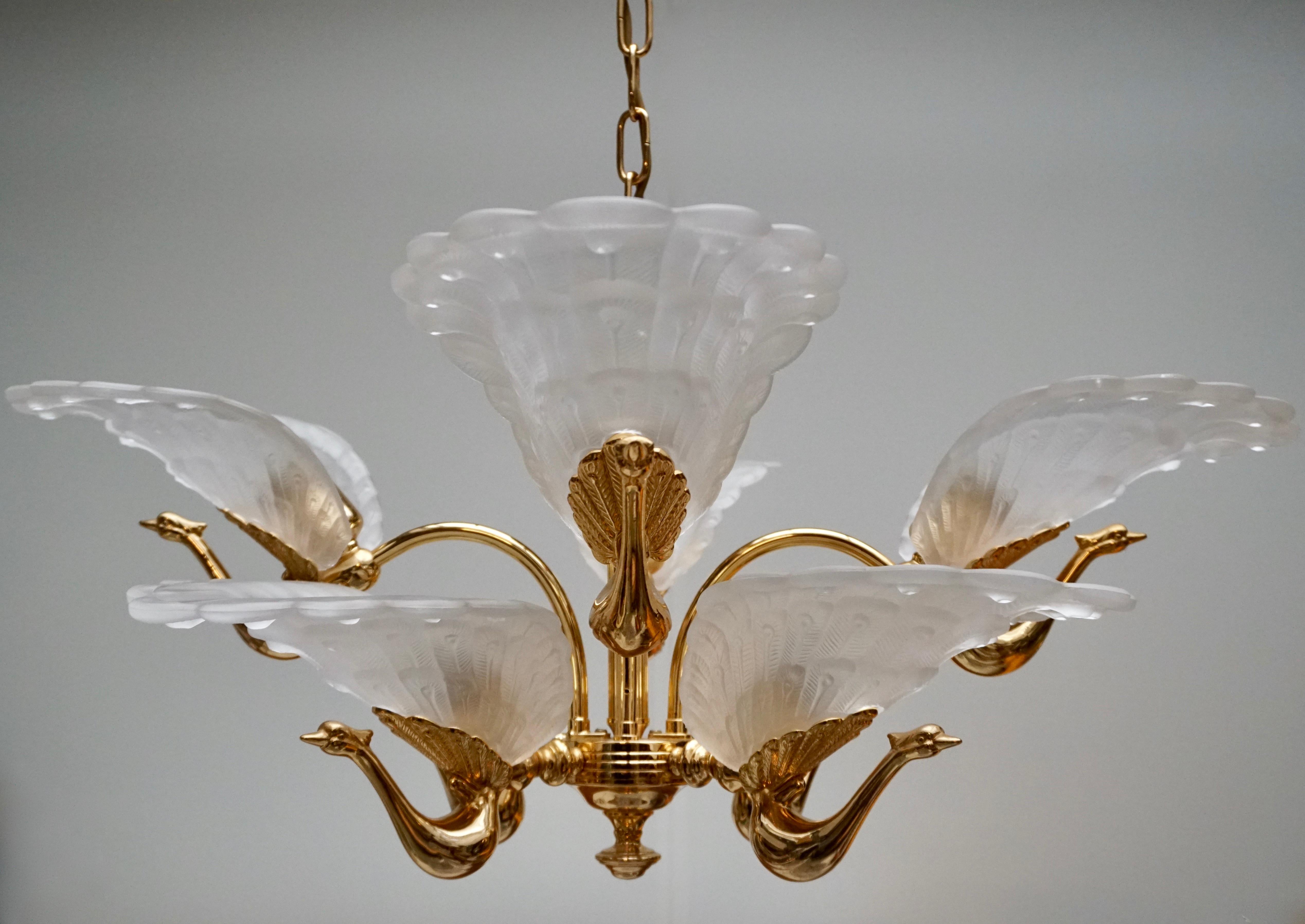 A eight light chandelier with eight etched or frosted glass shades, each embossed with a peacock motif. The cast metal bird's bodies and sculptured center column are heavy weight cast metal with an original lacquered brass finish. Sculptural and