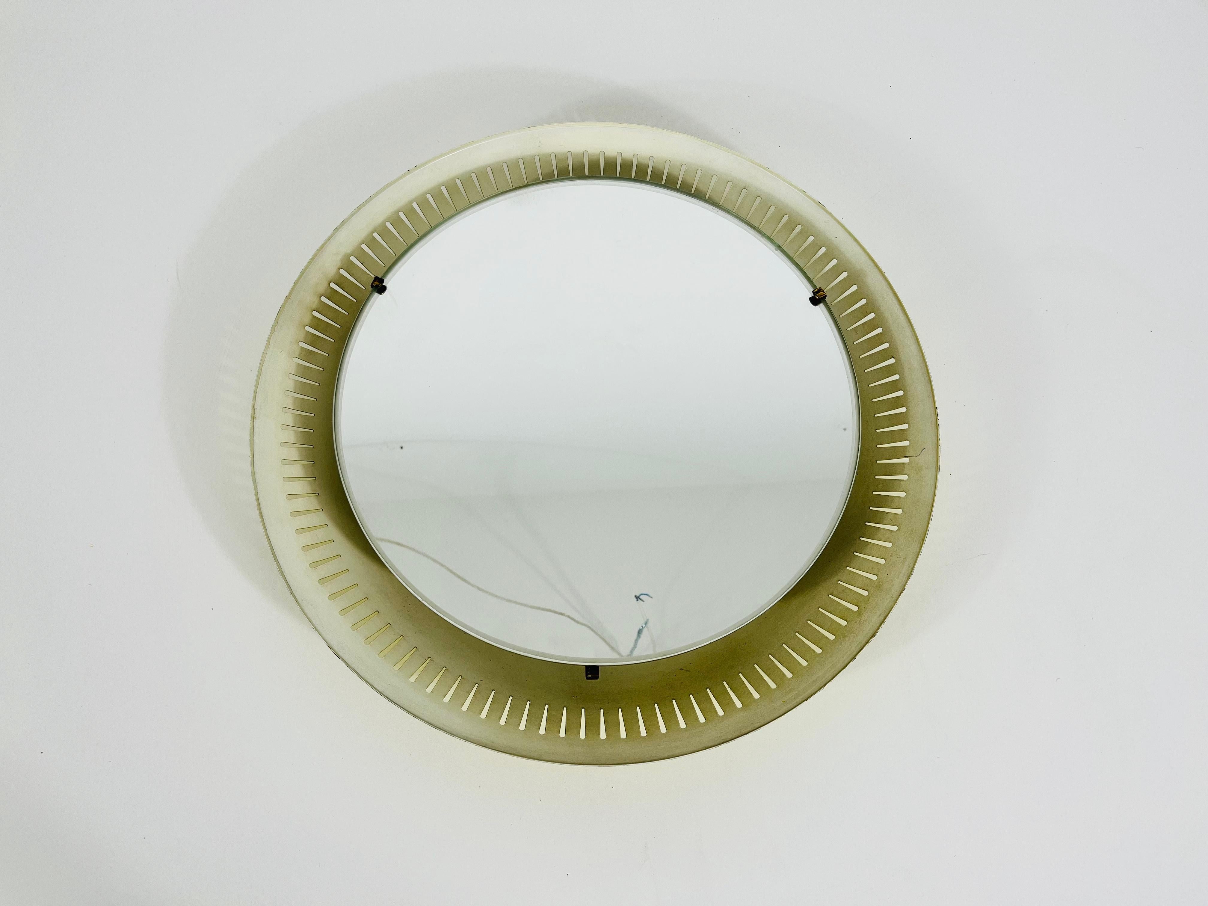 A Hillebrand illuminated wall mirror from the 1950s made in Germany. The mirror has a round metal design. There are E14 light bulbs inside the frame. Brass screws which secure the glass to the aluminium frame. 

The mirror is in a good vintage