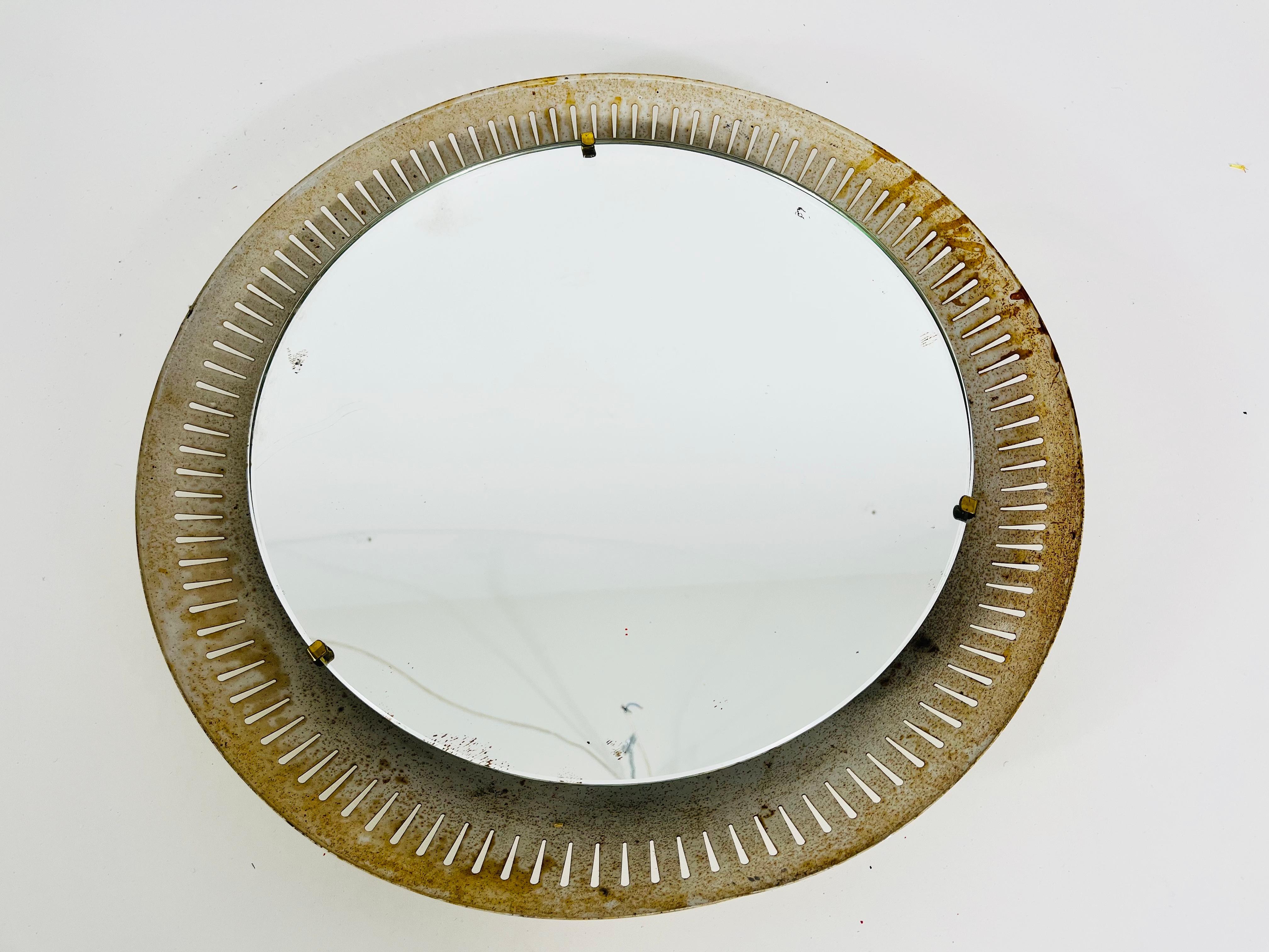 A Hillebrand illuminated wall mirror from the 1950s made in Germany. The mirror has a round metal design. There are E14 light bulbs inside the frame. Brass screws which secure the glass to the aluminium frame. 

The mirror is in a very used