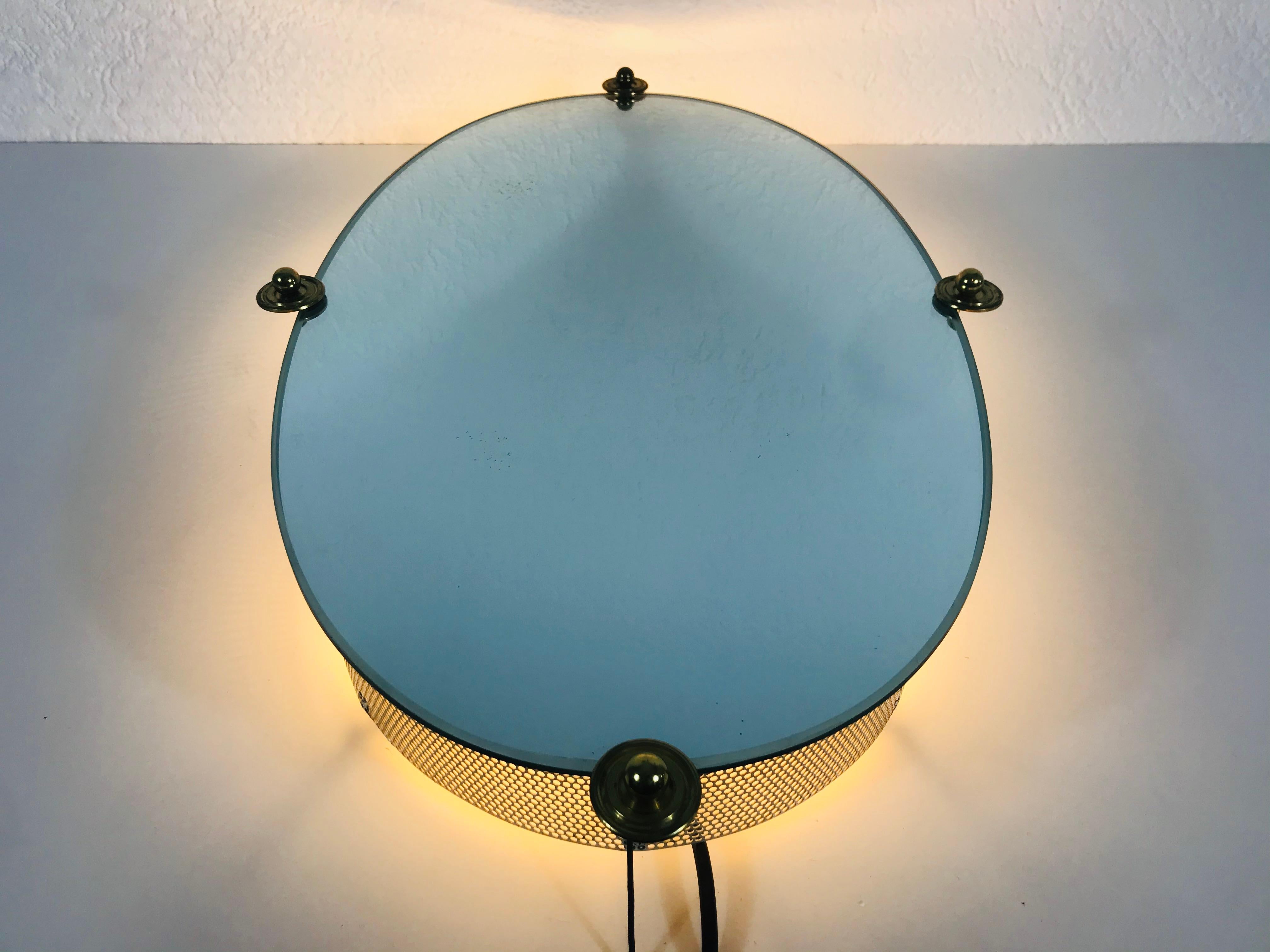 A Hillebrand illuminated wall mirror from the 1960s made in Germany. The mirror has an oval metal design. There are E14 light bulbs inside the frame. 4 brass screws which secure the glass to the aluminium frame. The mirror is in a good vintage