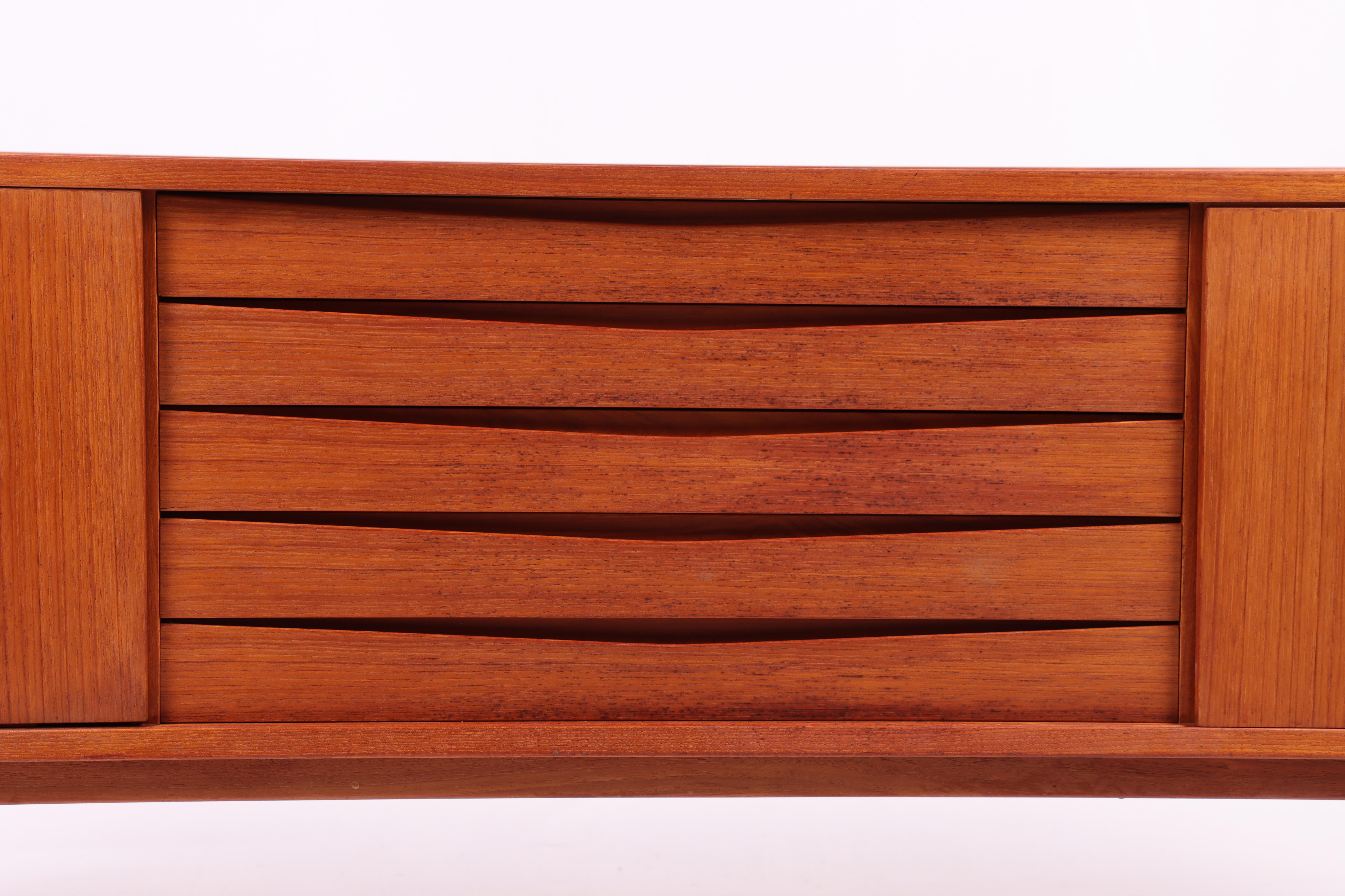 Beautiful sideboard from the 1960s, crafted in teak veneer with steel legs and teak shoes. Produced by Skovby Møbelfabrik, Denmark. The piece features two sliding doors with round recessed handles and a central section with sculpted drawers that add