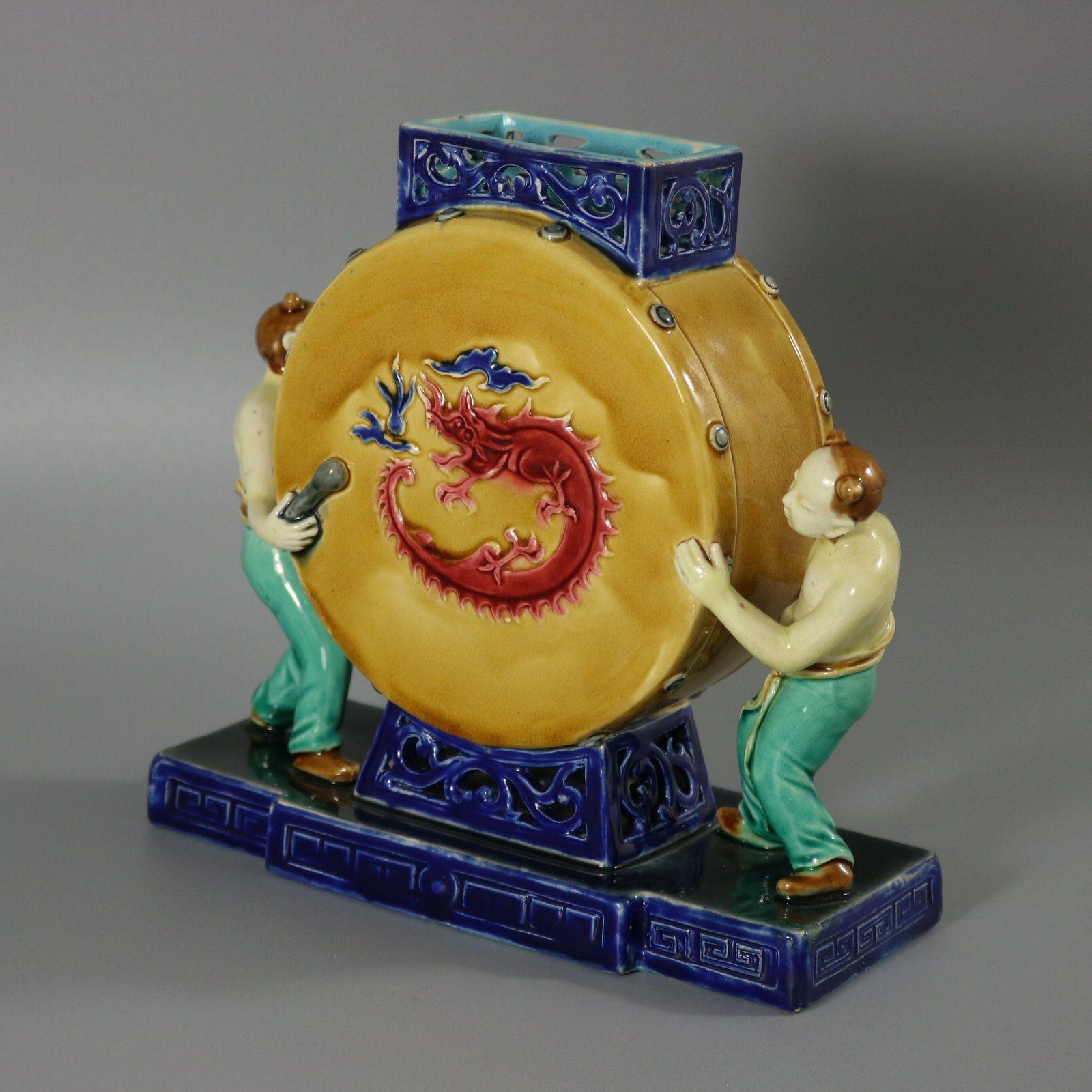 Minton Majolica vase which features a large drum with Chinese drummers stood either side. The drum has dragons on both faces. Intricate cut-out rim and base. Colouration: light brown, red, cobalt blue, are predominant. The piece bears maker's marks