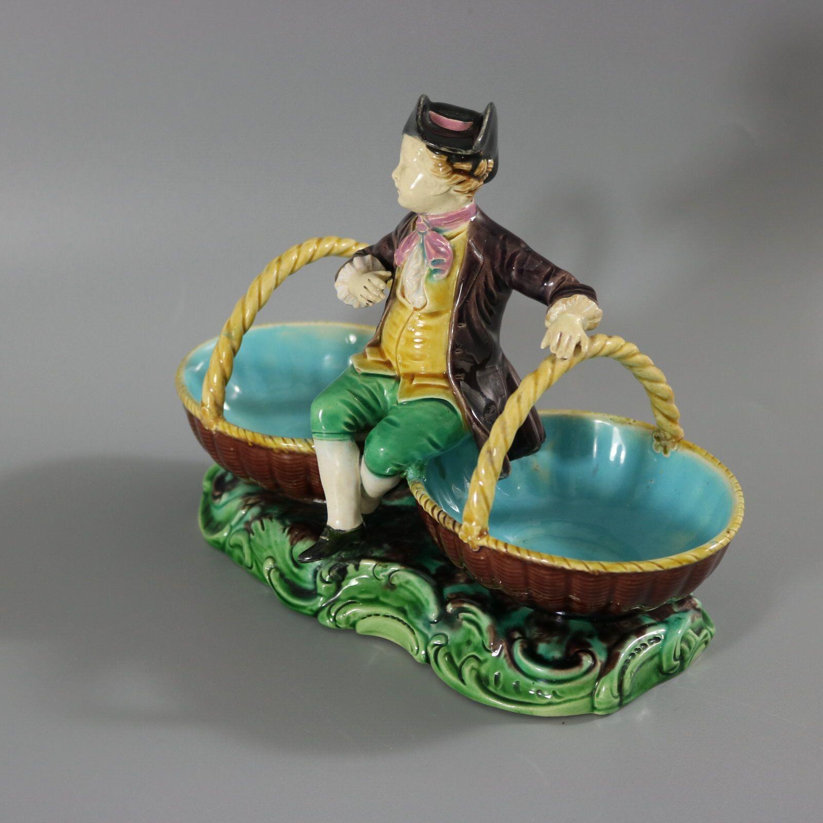 Plat en majolique de Minton représentant un jeune homme vintager, assis entre deux paniers. Coloration : les couleurs brune, verte et jaune sont prédominantes. La pièce porte les marques du fabricant de la poterie Minton. Les marques comprennent un
