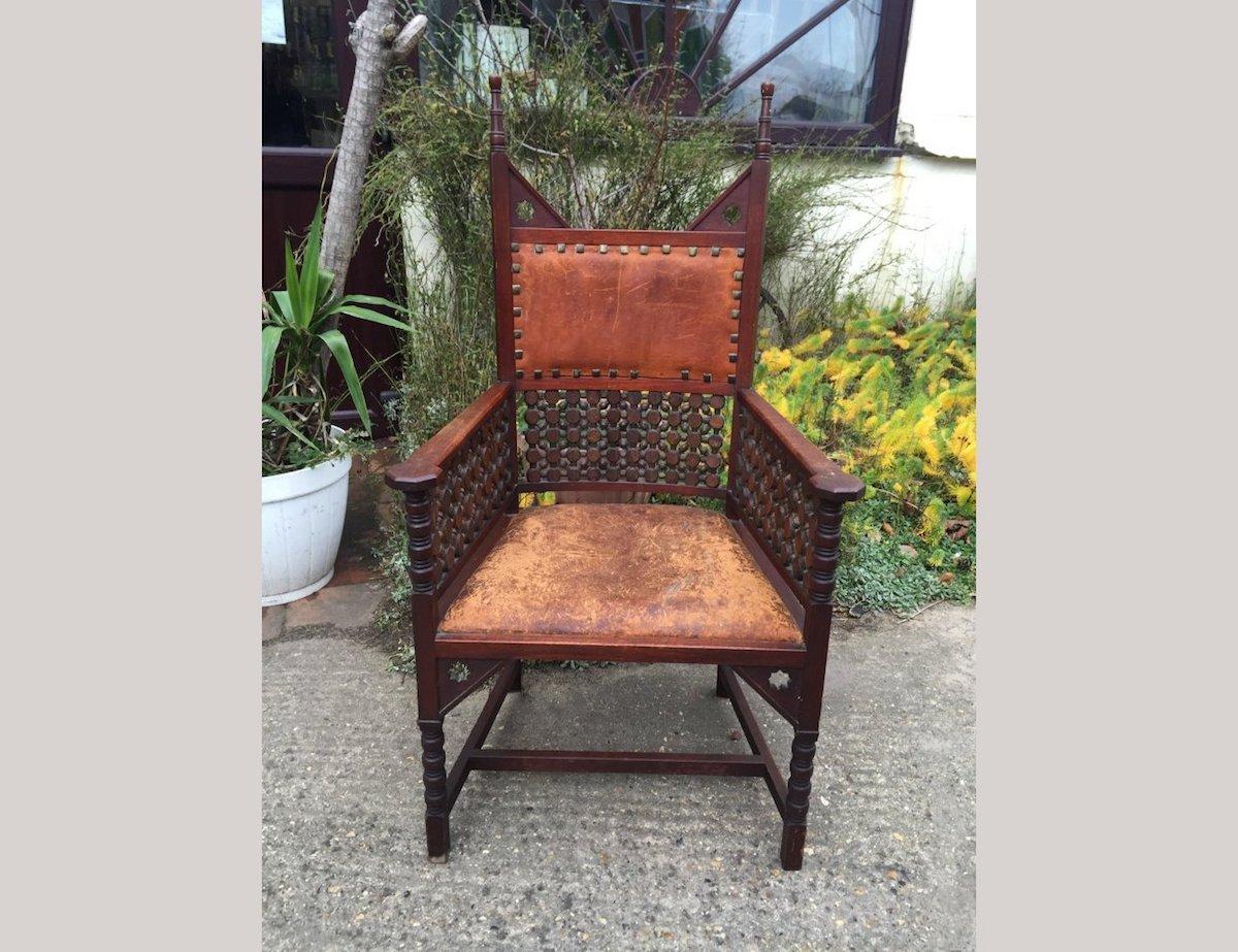 Liberty and Co. An Aesthetic Movement high-back Walnut armchair with elongated turned finials and triangular upper supports to each side pierced with Moorish devices. Under the shaped arms and under the leather backrest are Musharabieh turnings.